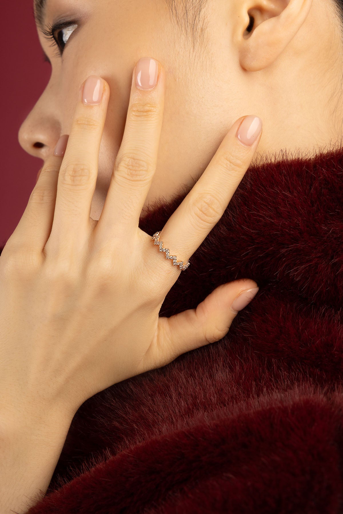 Woman wearing APM ring, a delicate zigzag shimmer against burgundy softness.