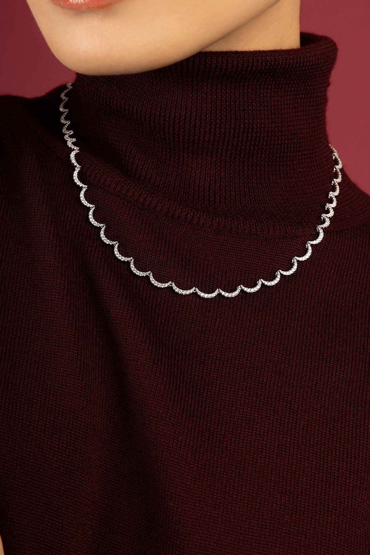 Woman wearing APM Monaco necklace, a scalloped shimmer against burgundy warmth.