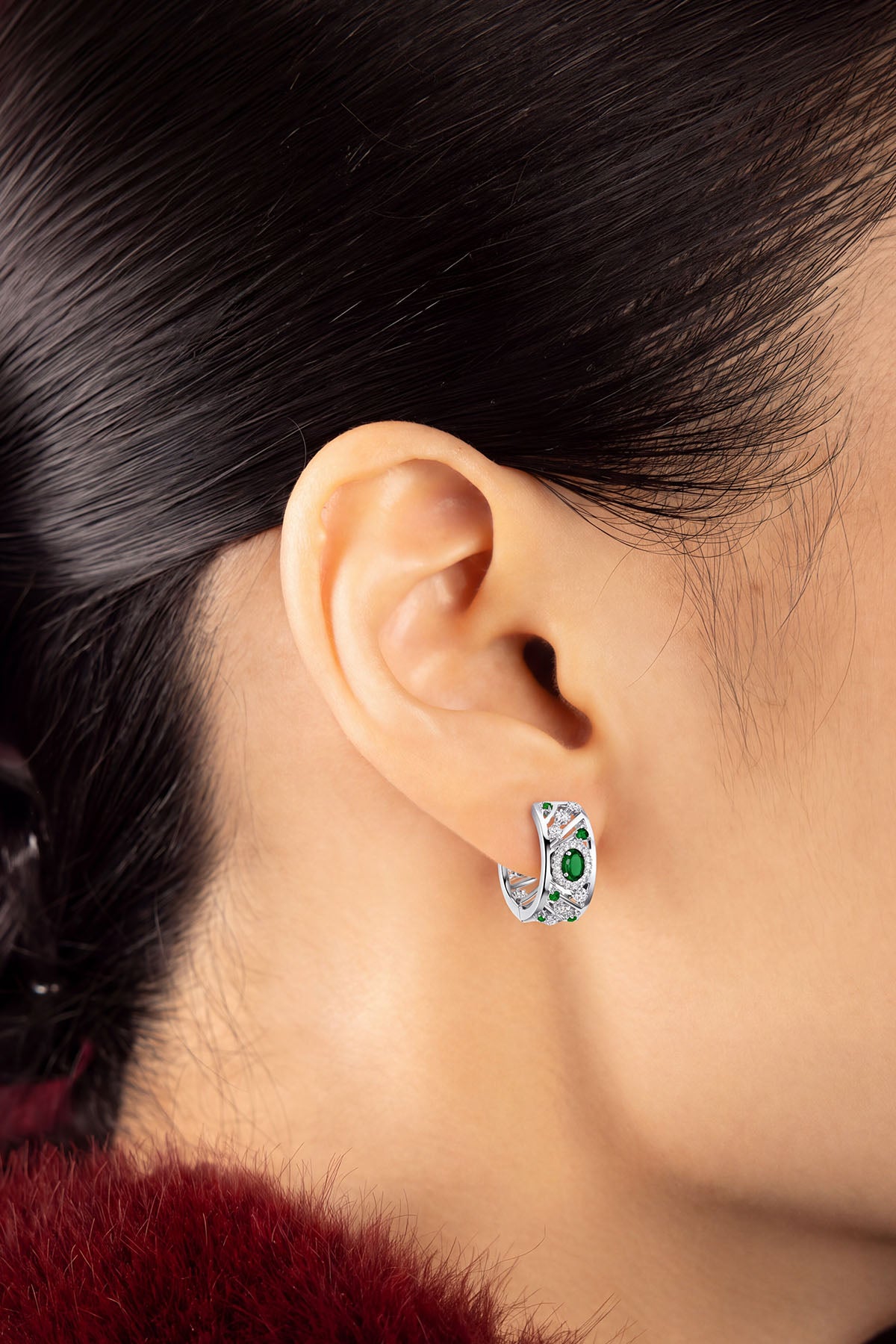 Woman wearing APM Monaco hoop earrings, emerald green glow with rhodium finish elegance.