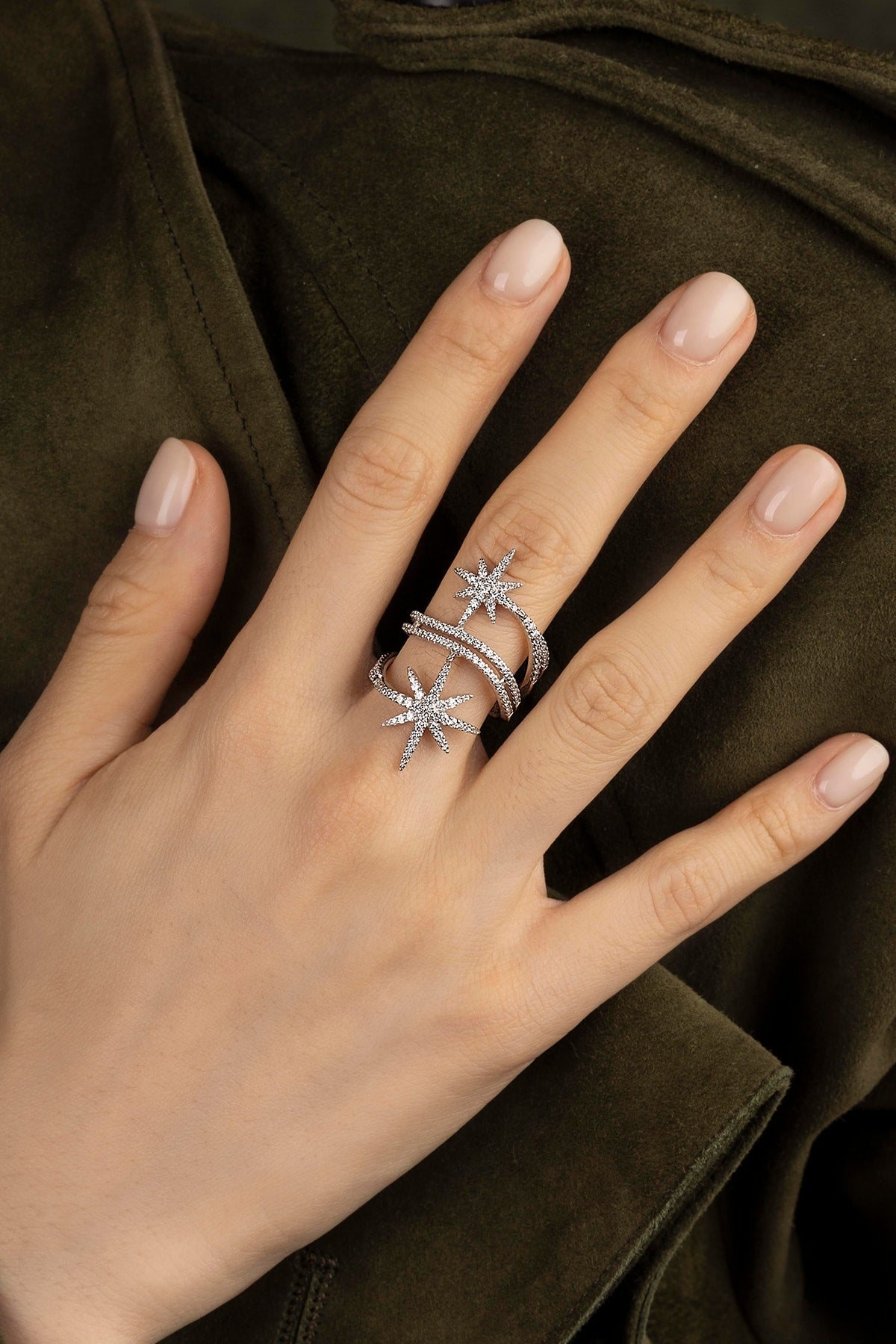 Hand wearing a silver star-shaped ring on a dark background