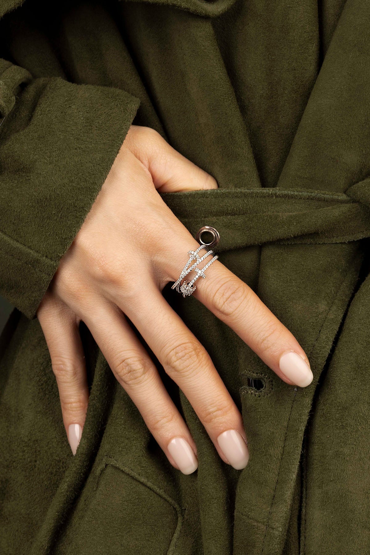 Hand wearing multiple rings on a green coat background