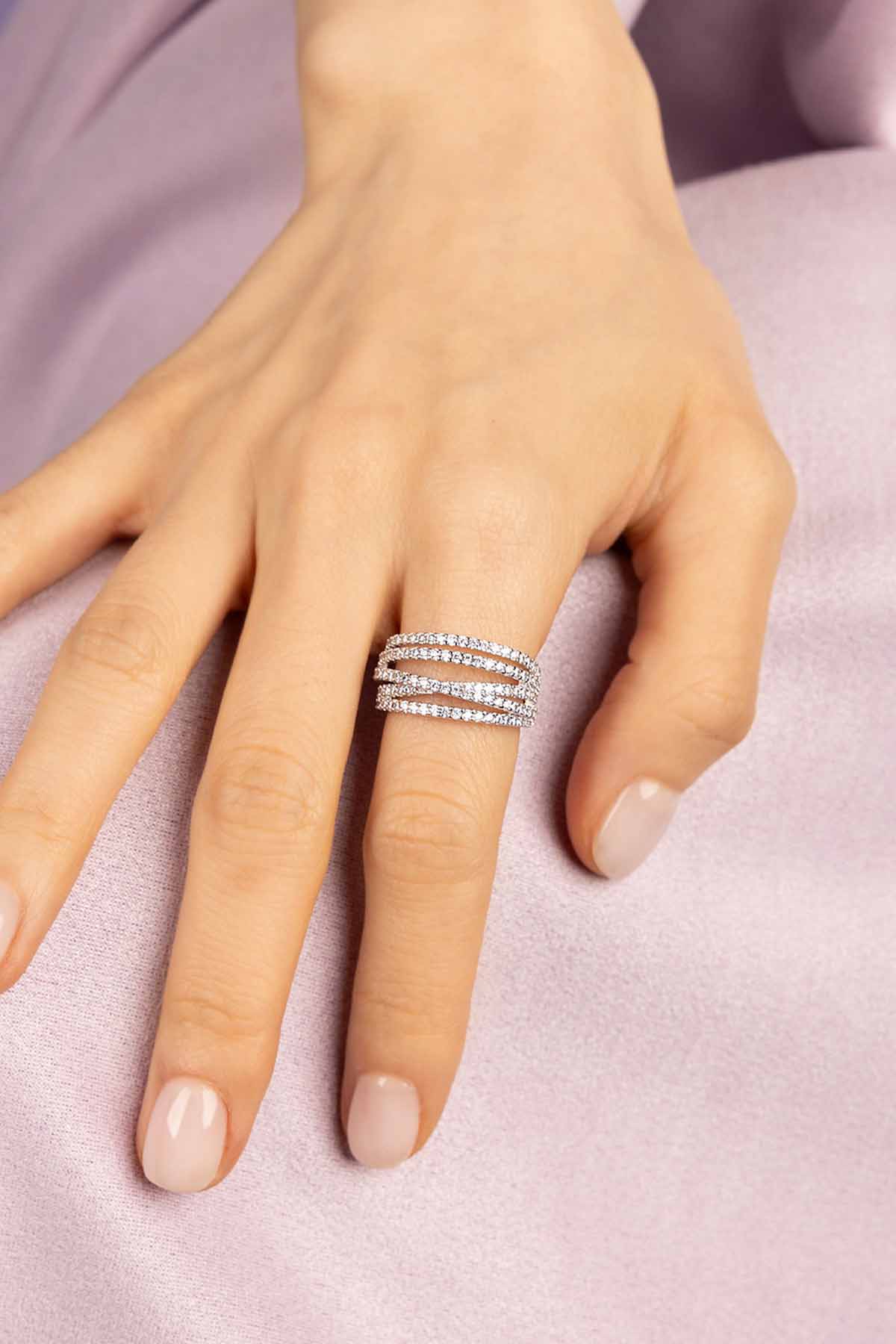 Hand wearing APM MONACO silver rings with five-hoop design on a purple background