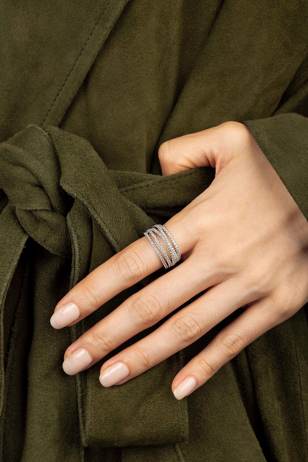 Hand wearing a silver ring on an olive green fabric background