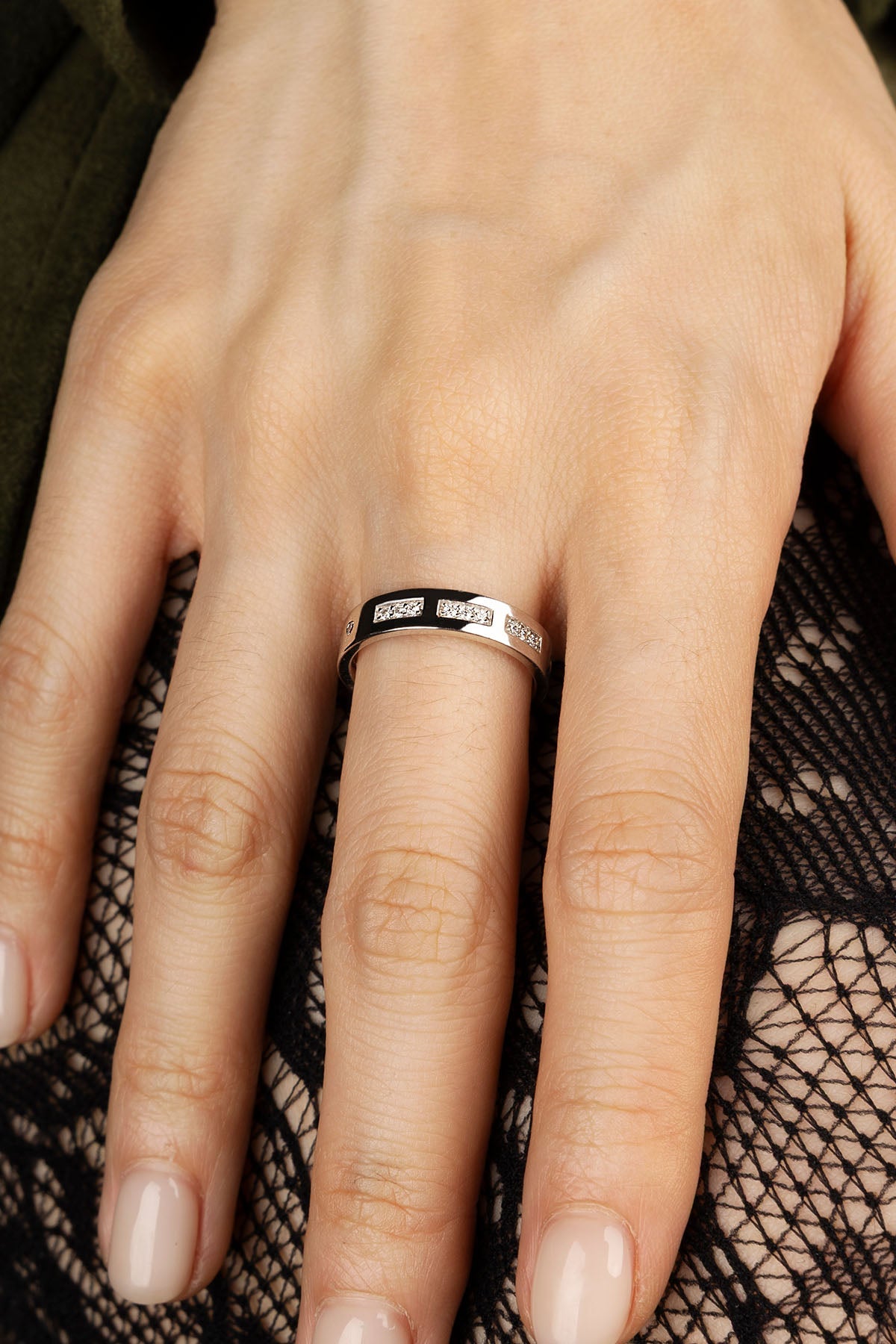 Hand wearing a silver ring with black interior on a black lace background