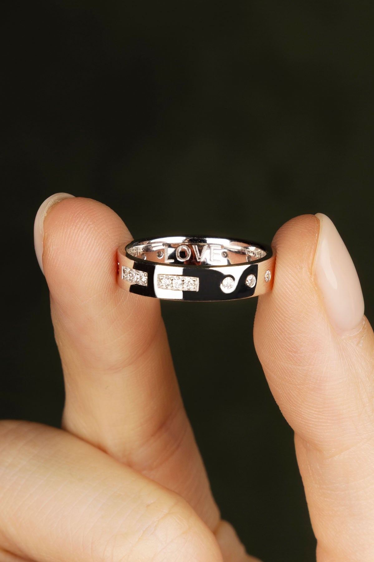 Silver ring with 'LOVE' engraving held between fingers against a dark background