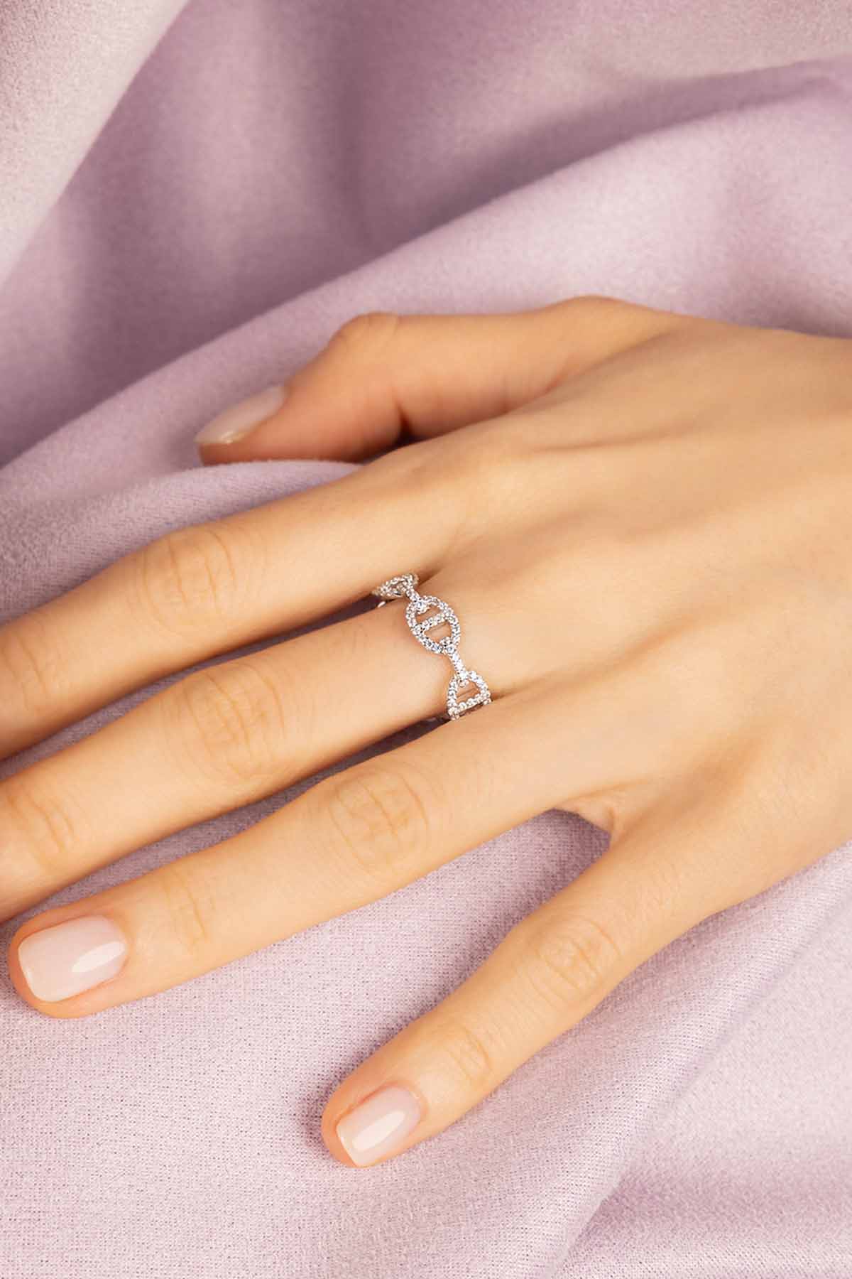 Hand wearing a silver ring with a cubic zirconia on a soft pink fabric background