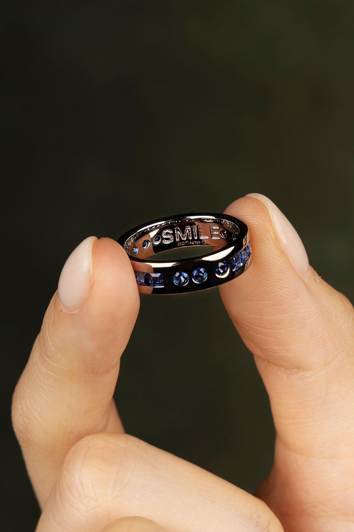 Person holding a black ring with blue gemstones and 'LOVE' engraving against a dark background
