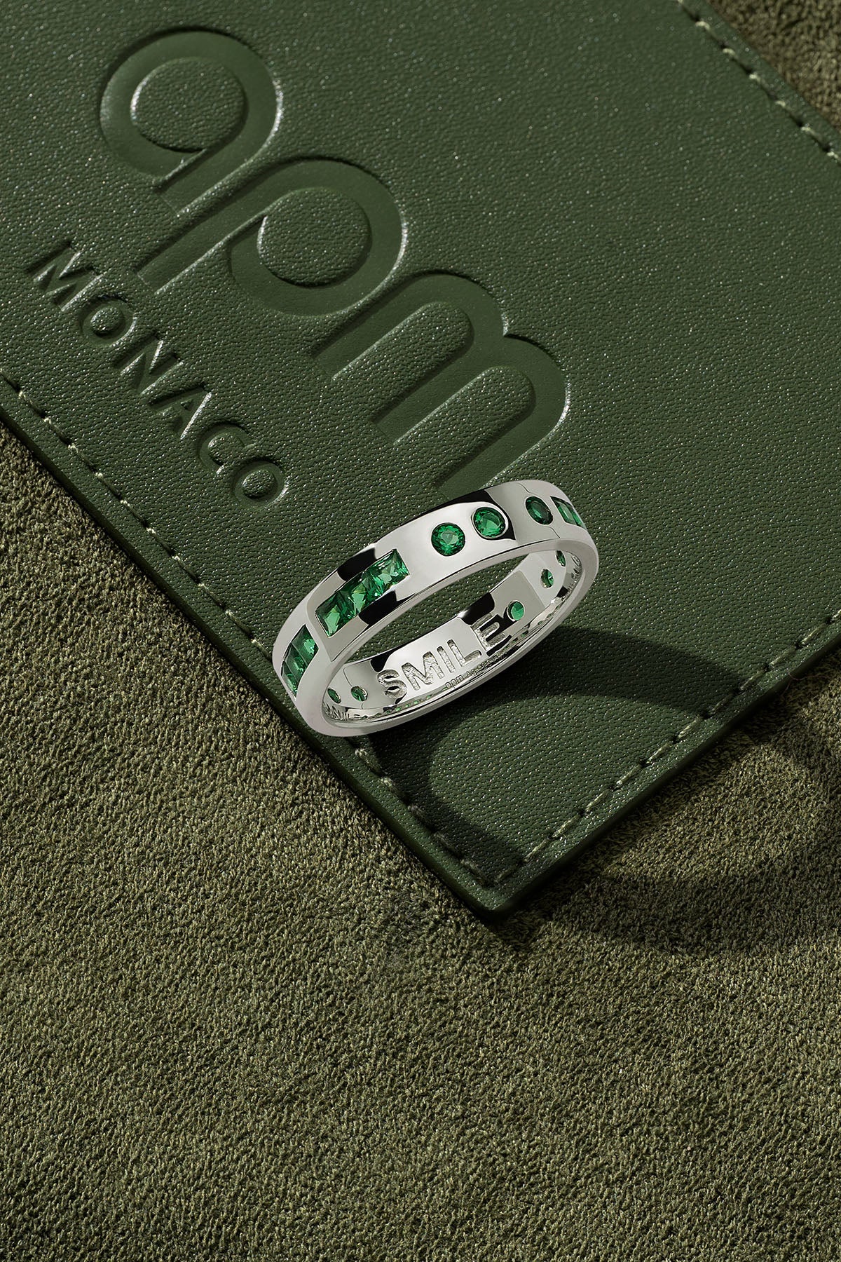 Silver ring with green stones on a green leather surface
