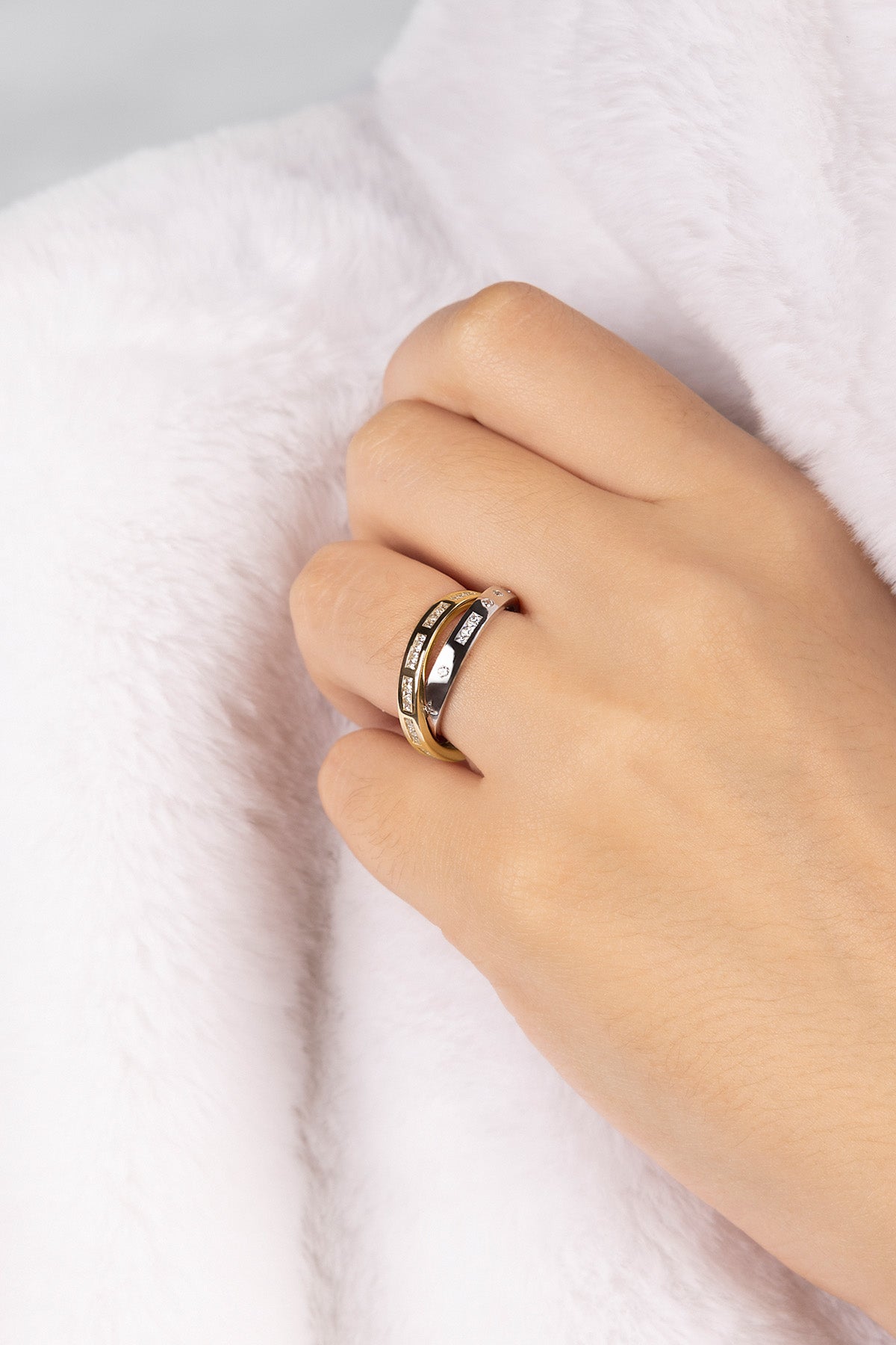 Hand wearing a gold and silver ring on a white fabric background