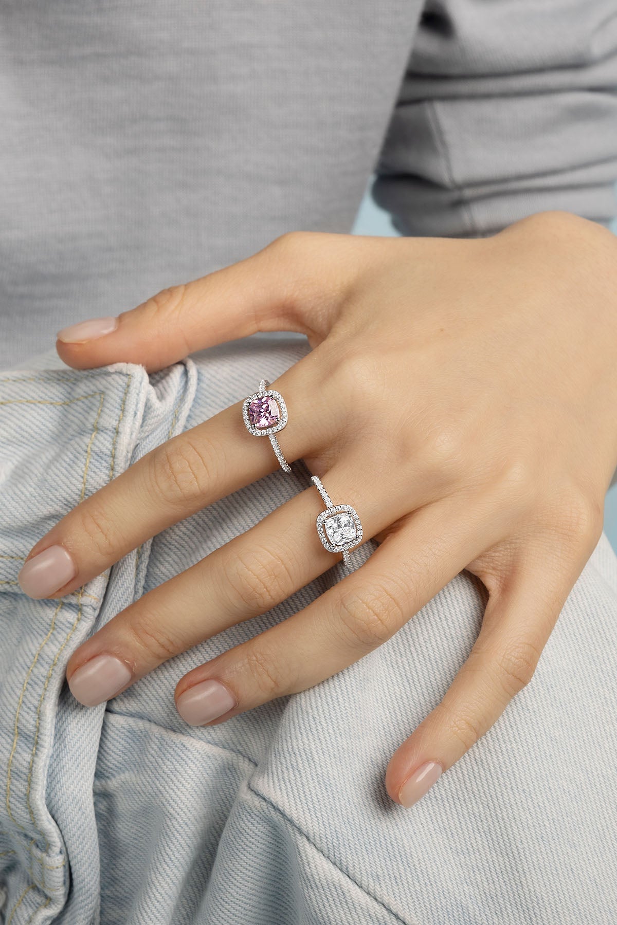 Rings APM Monaco. White-tone cushion-cut halo rings with pink and white center stones worn on two fingers.