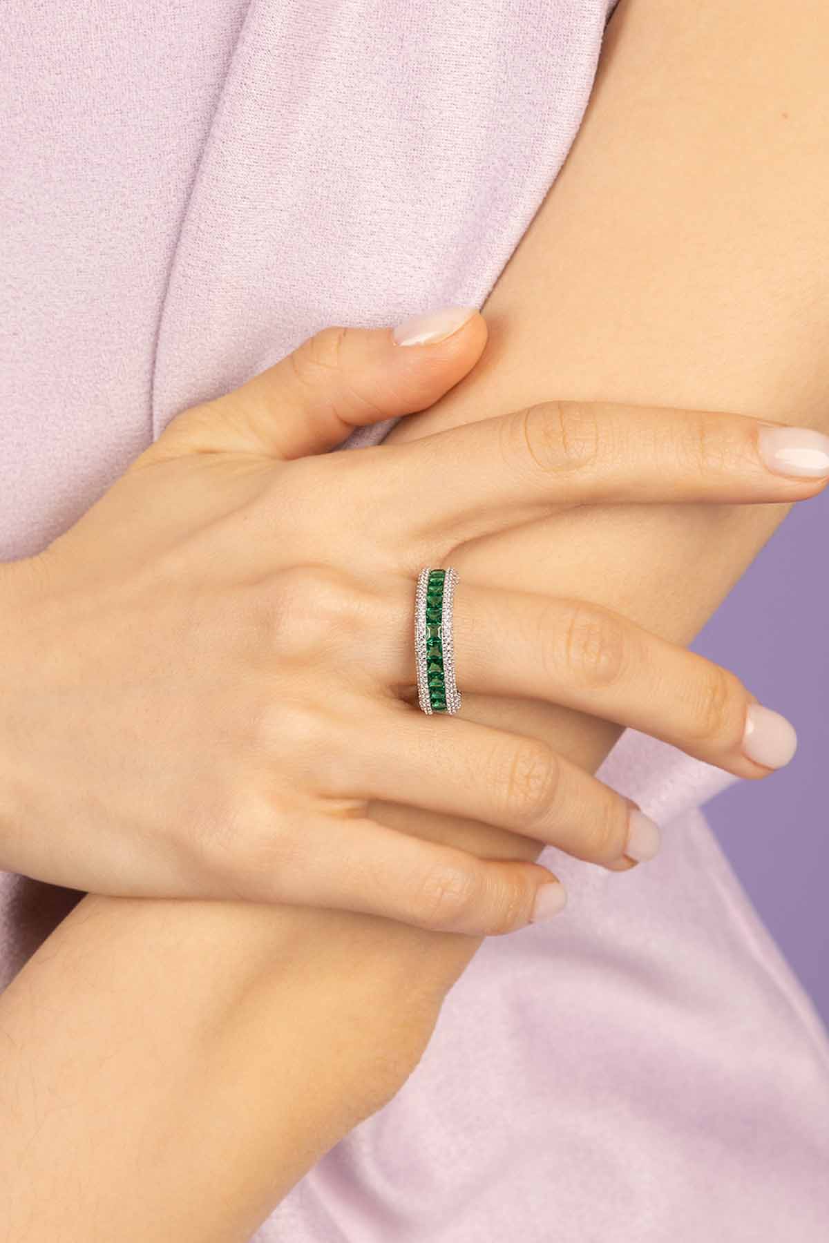 Close-up of a hand wearing a green and white ring on a light purple background
