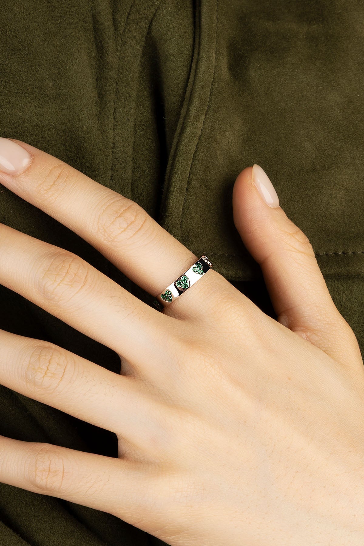 Close-up of a hand wearing a silver ring with green stones on a dark fabric background