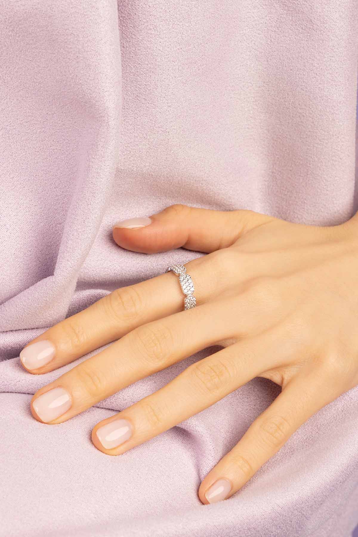 Hand wearing a zirconia ring on a soft pink fabric background