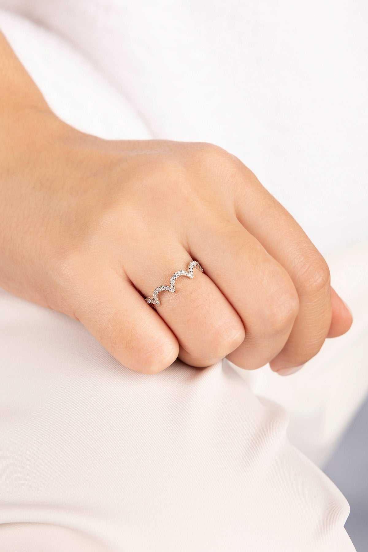Silver ring with small stones on a person's finger against a white background