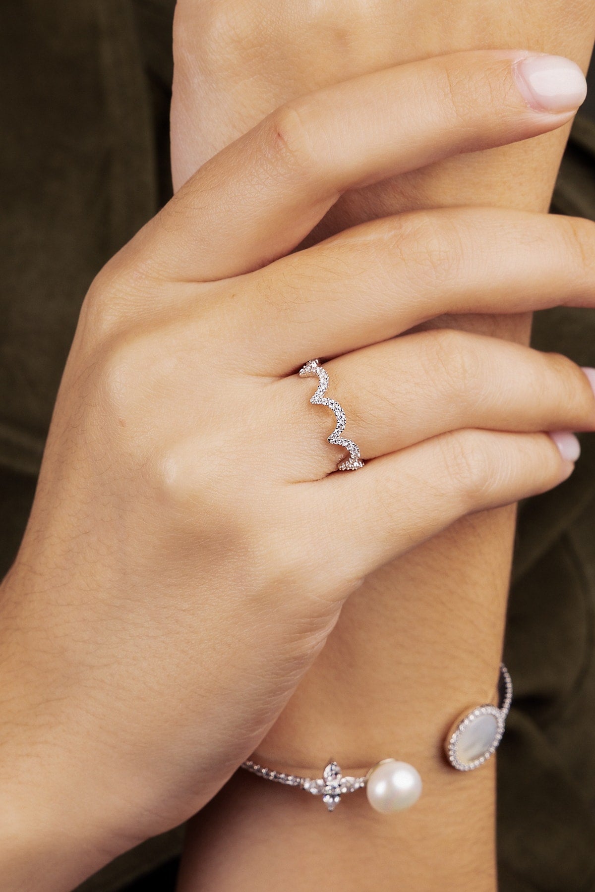 Close-up of a hand wearing a silver ring with a wave design and a bracelet.