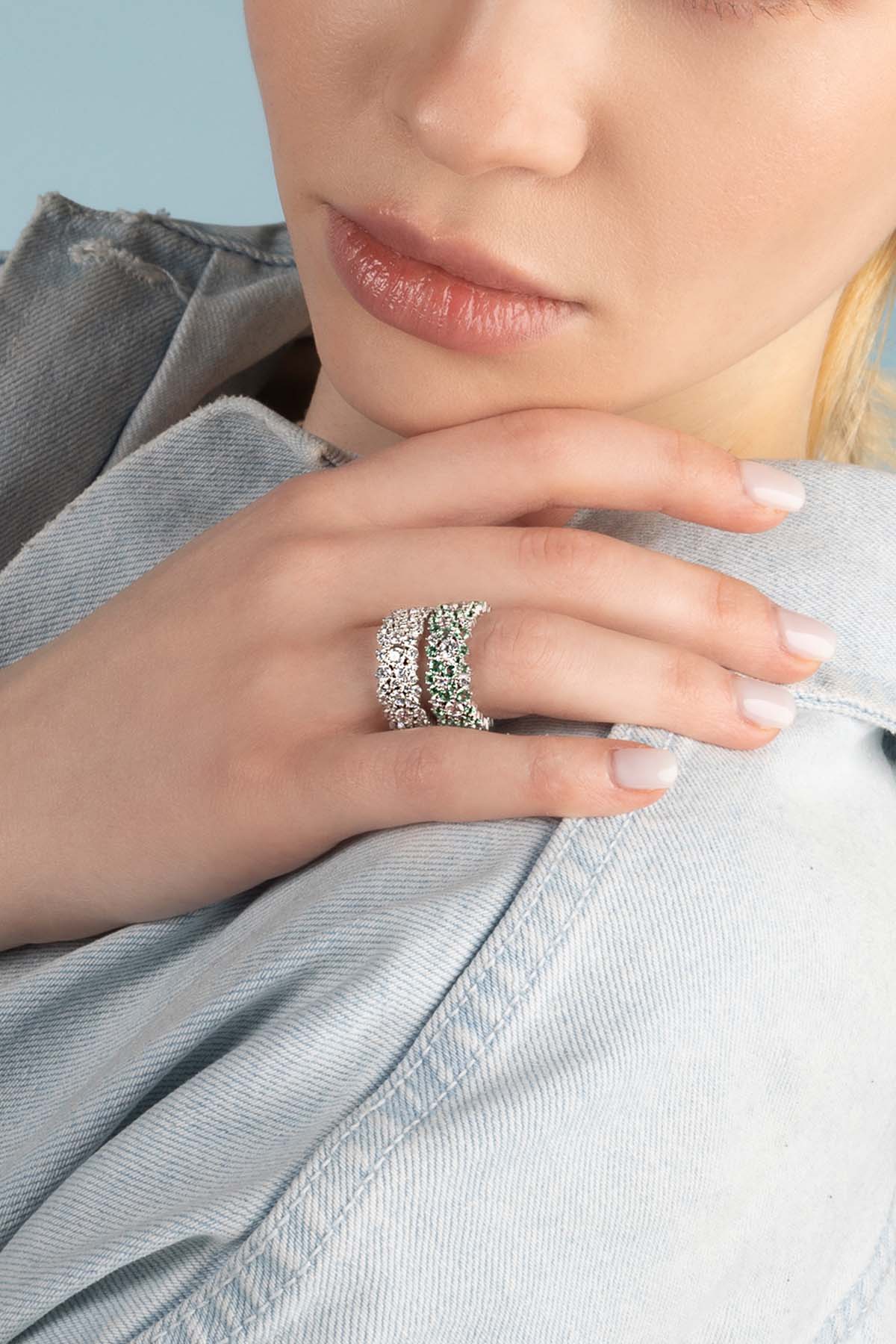 Rings APM Monaco fashion jewelry featuring two rings on the right ring finger: one diamond-studded and one emerald-stone, set in white metal.