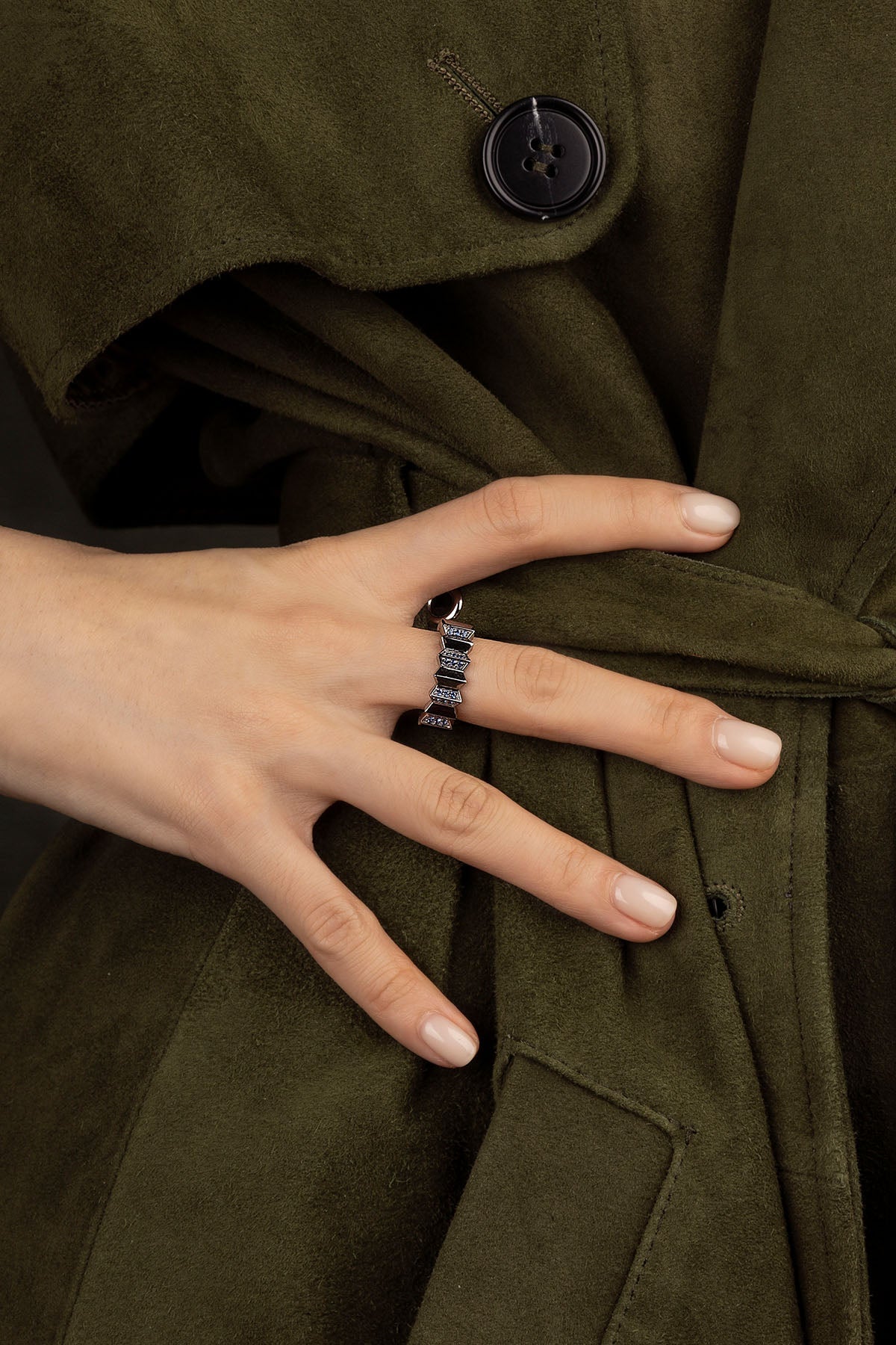 Hand wearing a APM Monaco Up and Down Ring in Dark Grey on a dark green coat background