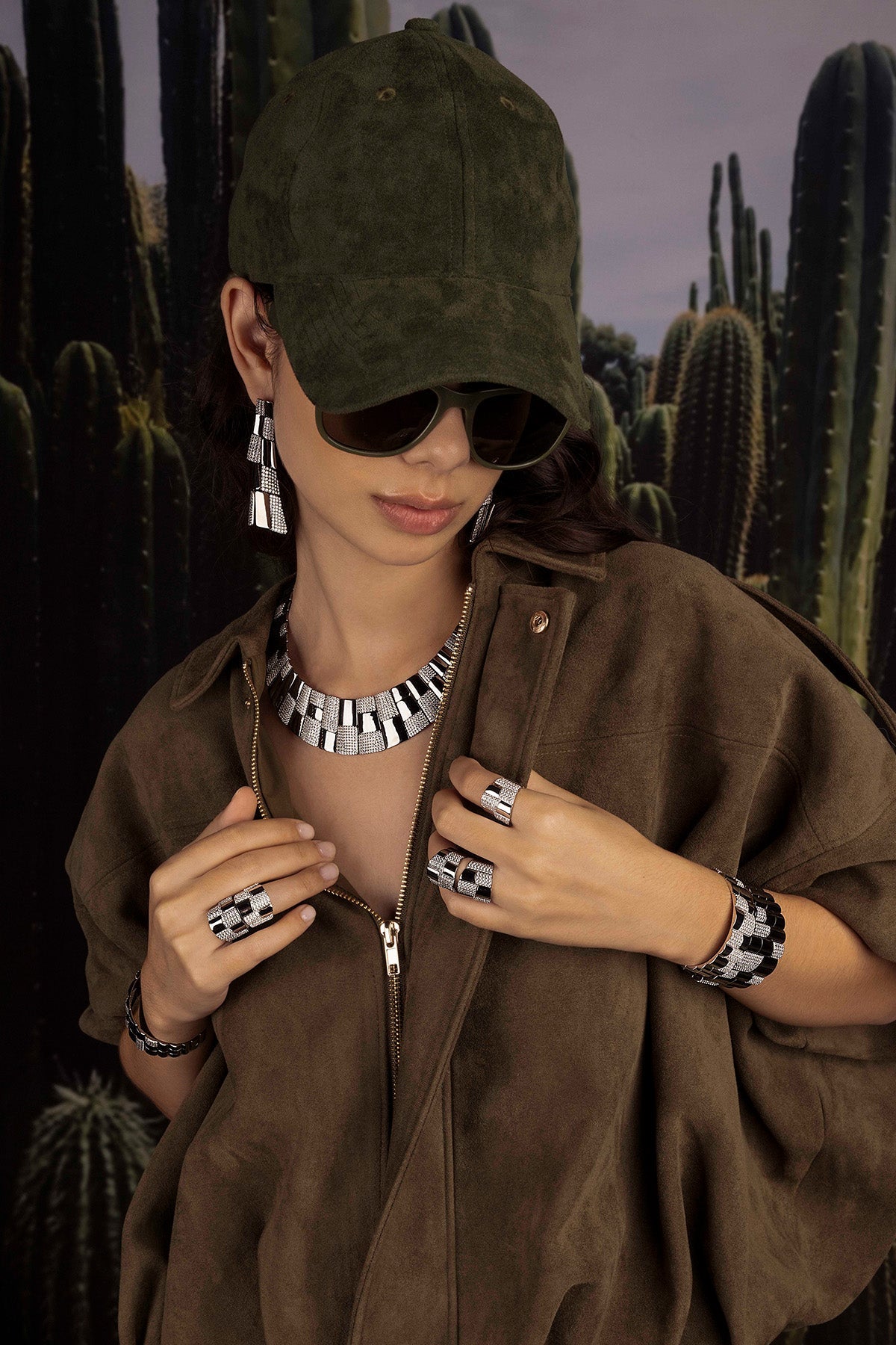 Model wearing a brown outfit with jewelry in front of cacti