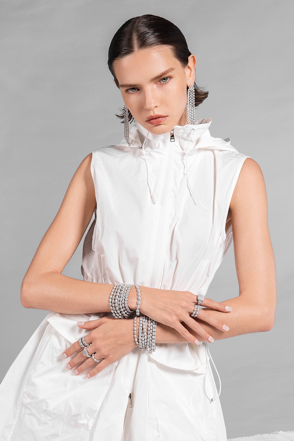 Model wearing a white sleeveless skirt with APM MONACO pave jewelry on a gray background