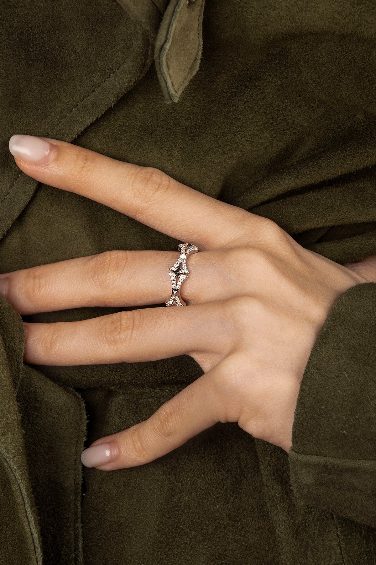 Hand wearing a APM Monaco Cross Ring ring with a green garment in the background