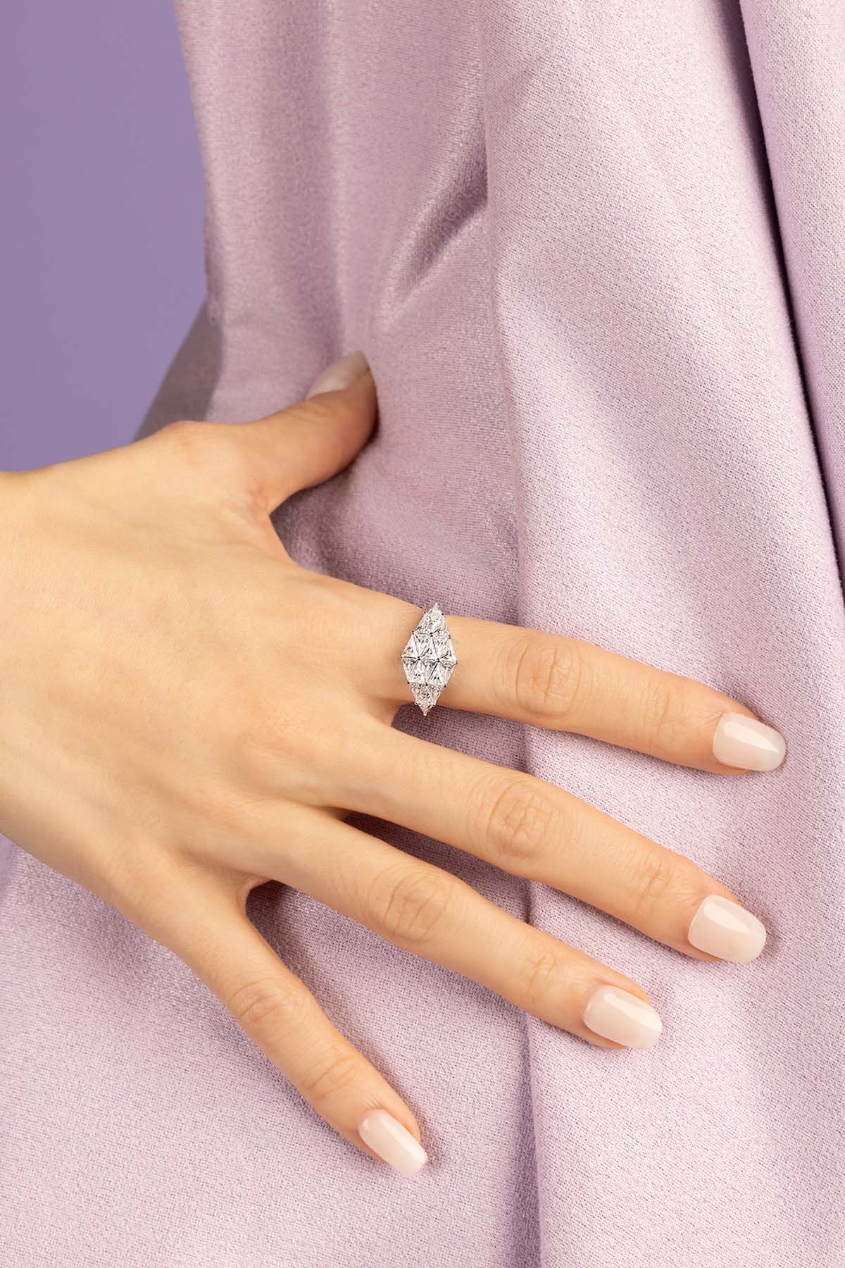 Hand wearing a zirconia ring on a soft purple fabric background
