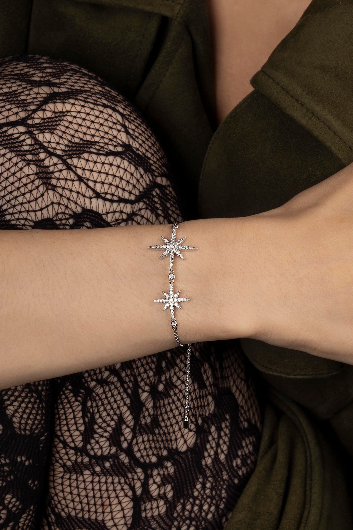 Silver bracelet with star designs on a wrist, wearing a green garment and black lace fabric.