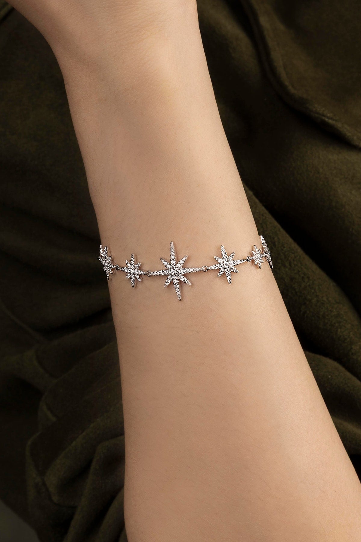Silver bracelet with star designs on a wrist against a green dark background