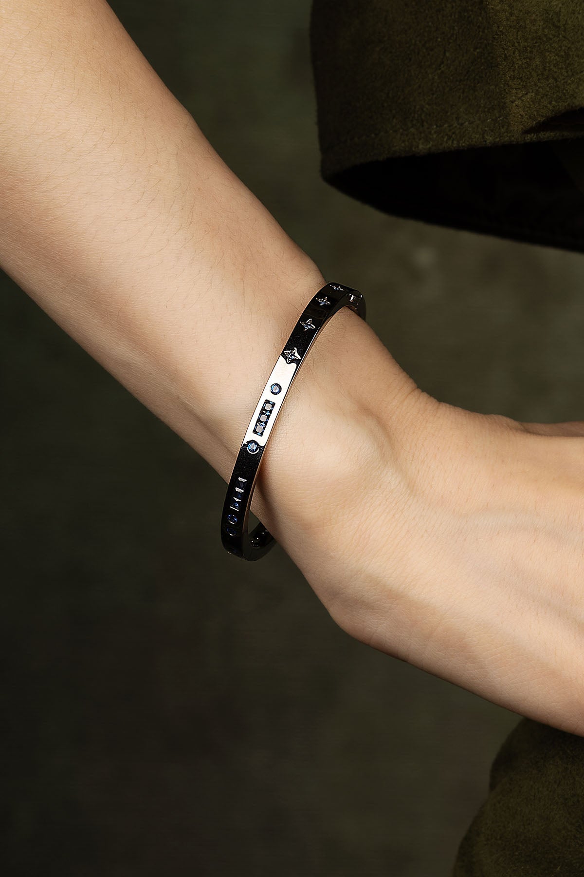Close-up of a wrist wearing a black bracelet with engraved designs on a dark background