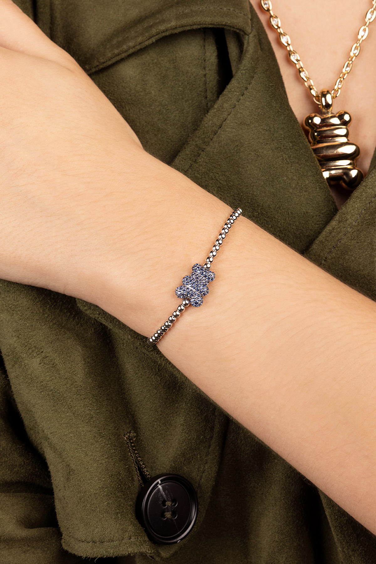 Bracelet with a blue yummy bear gemstone worn on a wrist, with a green garment in the background