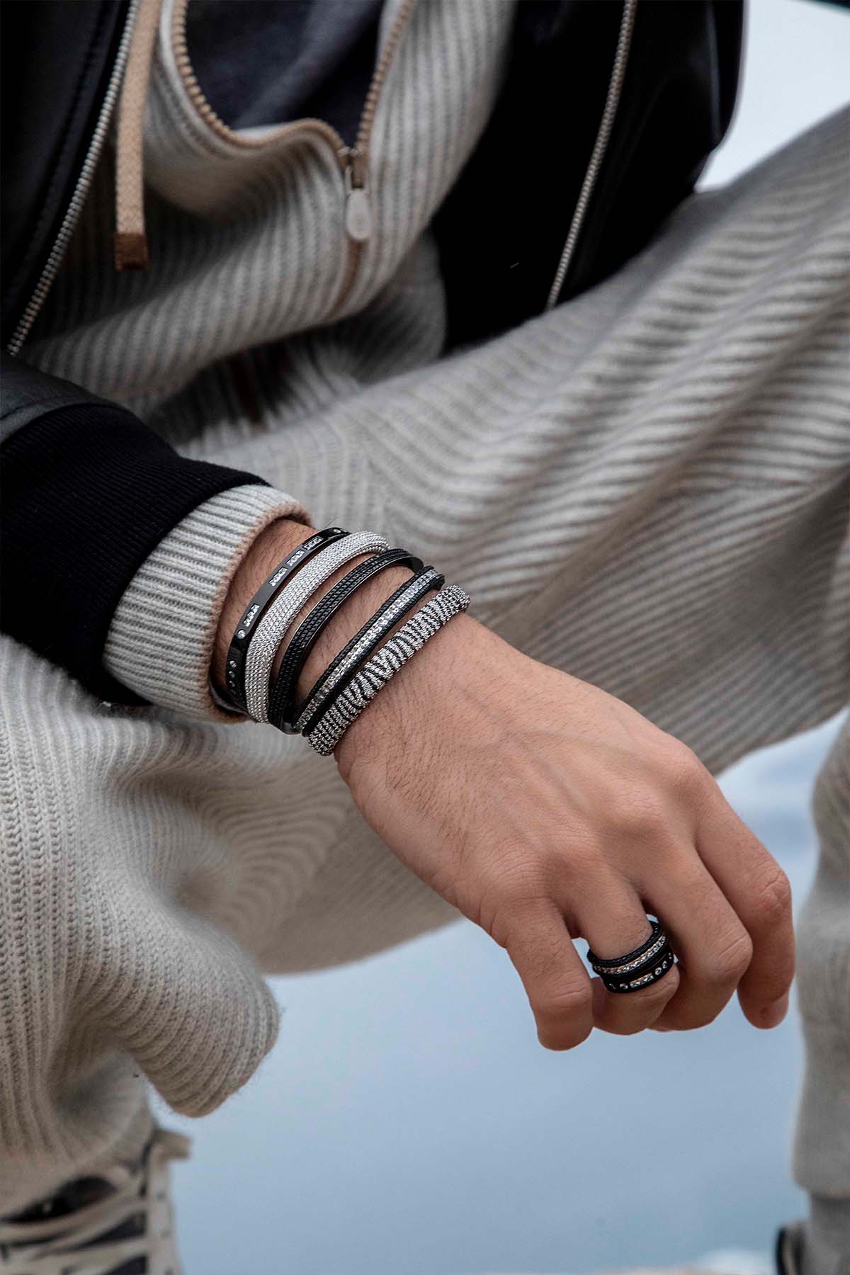 Bracelets APM Monaco: black and silver zebra-pattern bangles stacked on the left wrist, with a matching ring on the left hand; metal finish, no visible stones.
