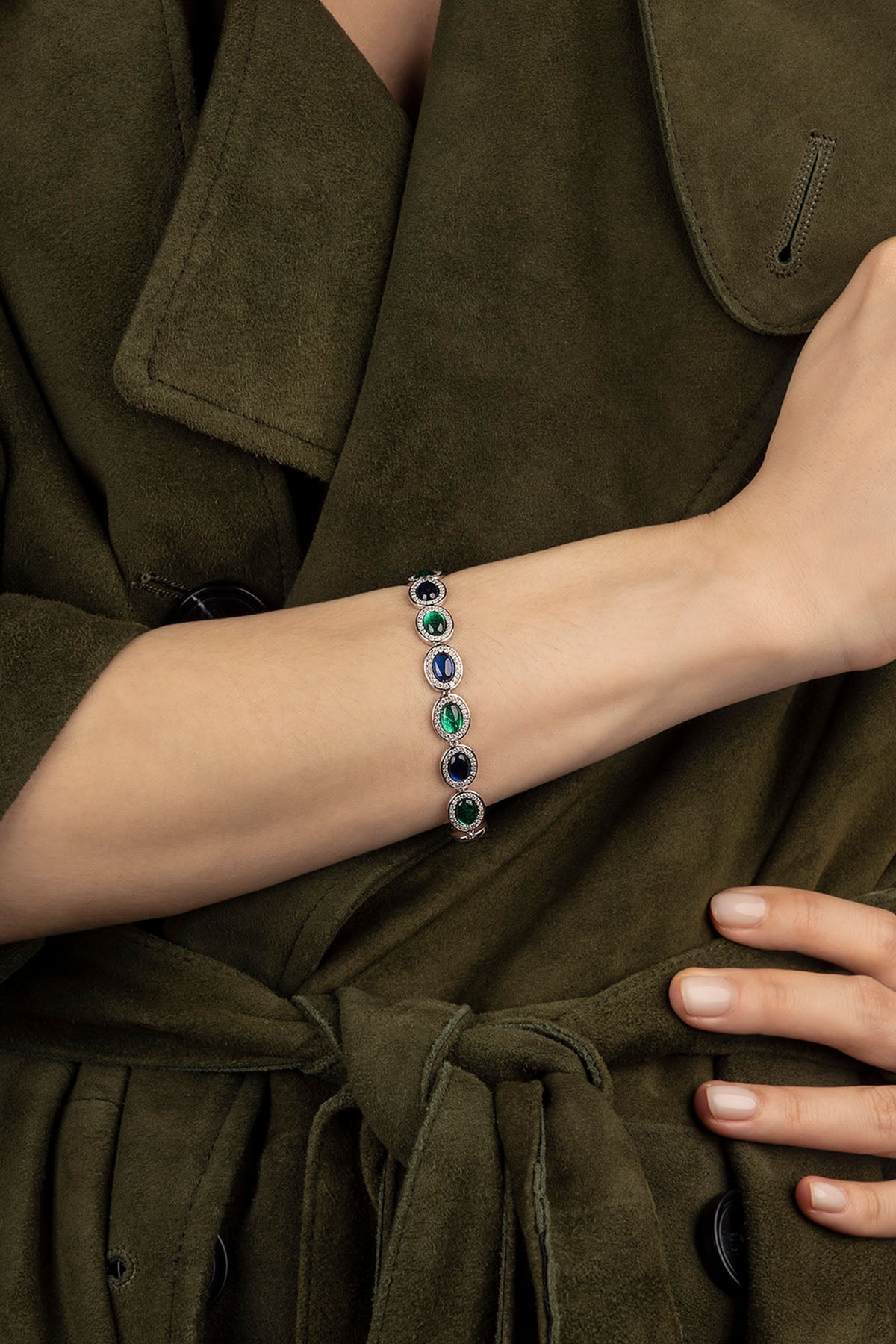 Close-up of a person wearing a bracelet with green and blue stones on an olive green coat.