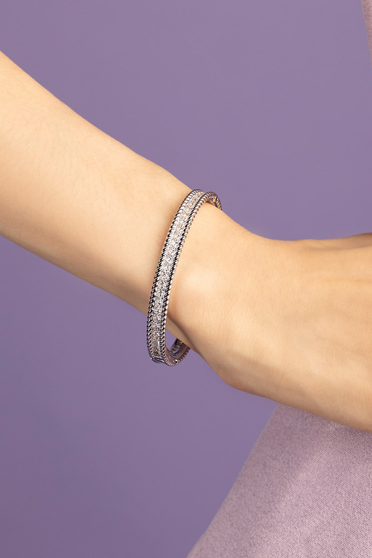 Silver bracelet on a person's wrist against a purple background