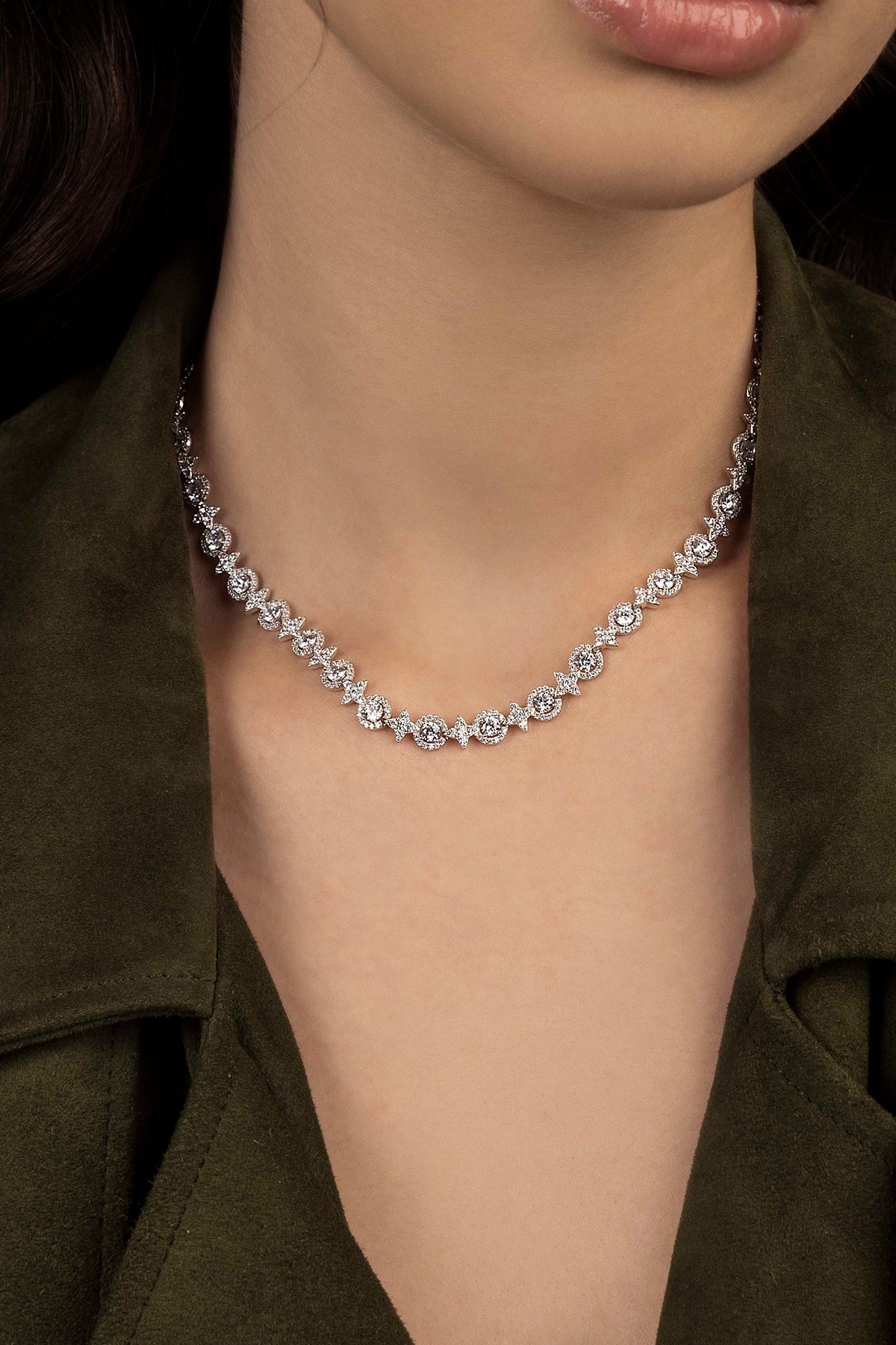 Close-up of a diamond necklace on a person wearing a green jacket.