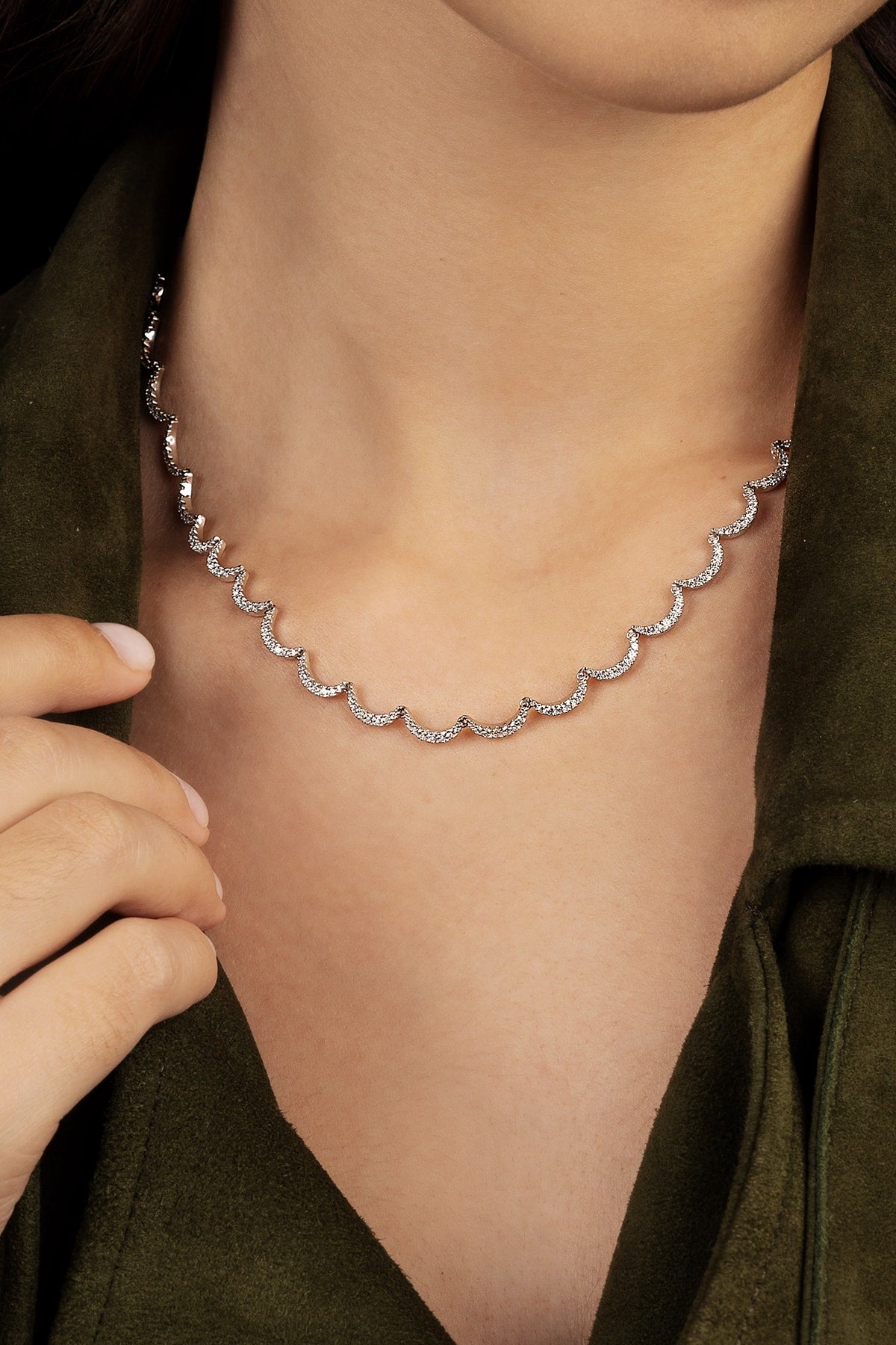 Silver necklace being worn on a model's neck with a green background