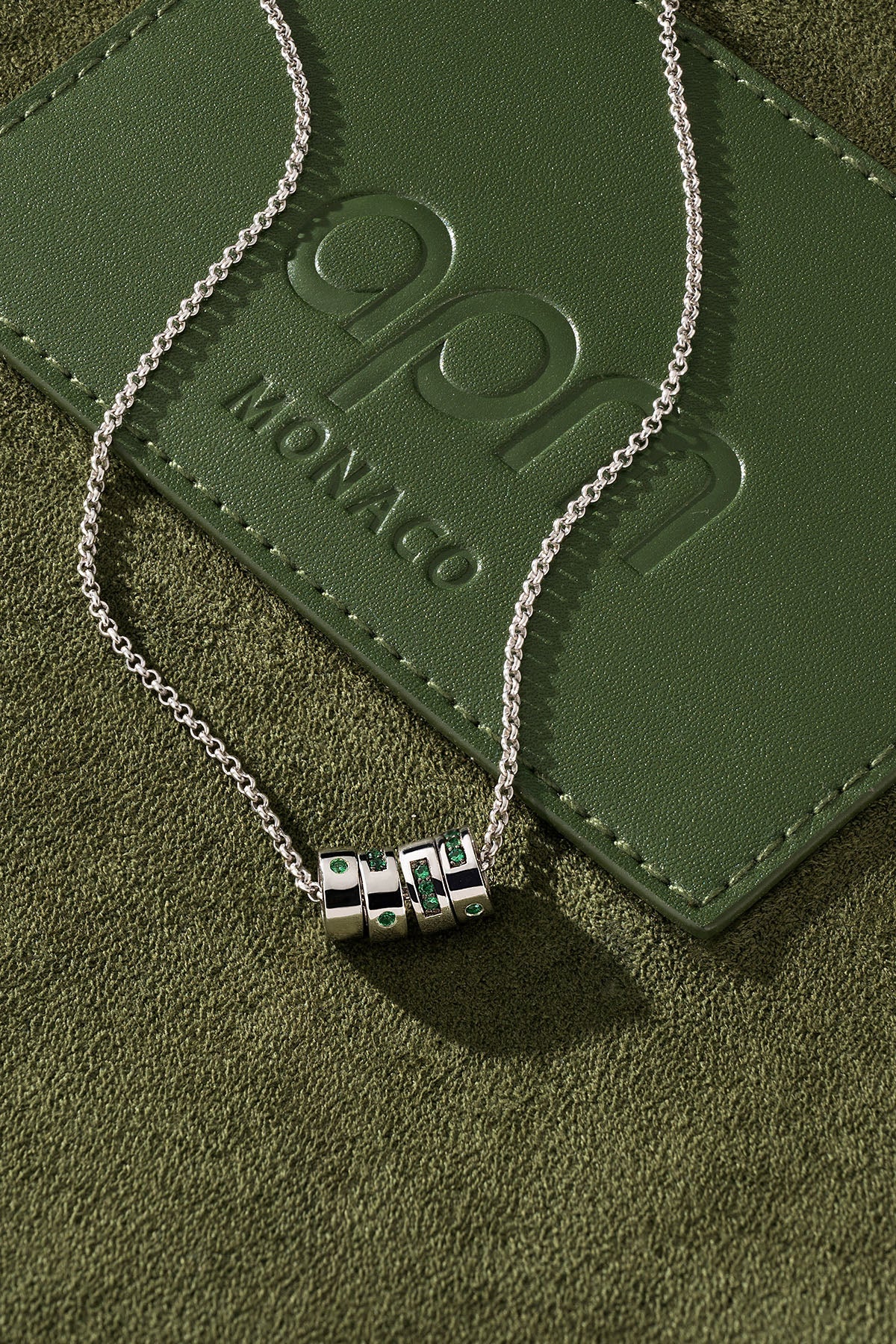 Silver necklace with a pendant on a green leather surface.