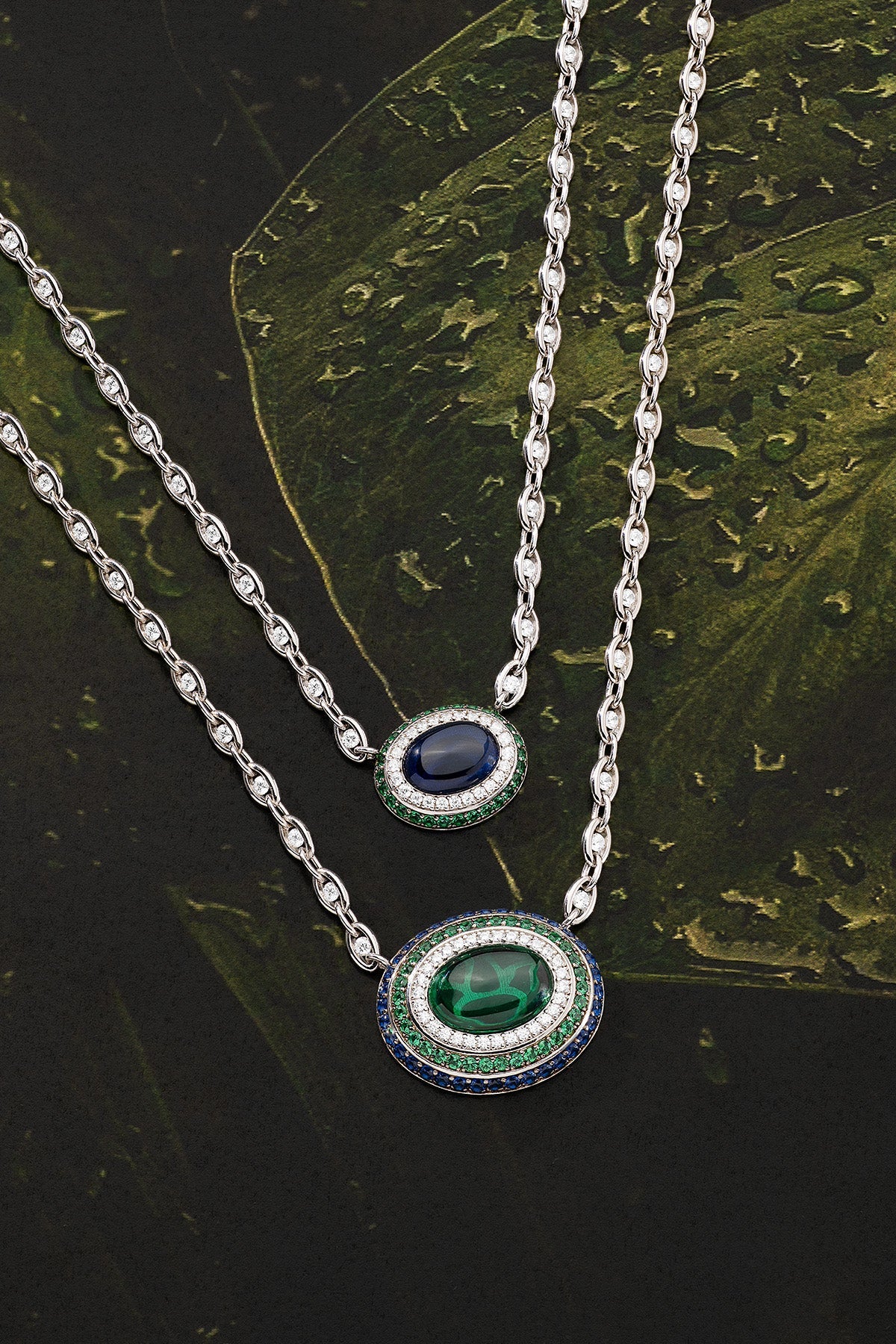 Two silver necklaces on a dark green leaf background