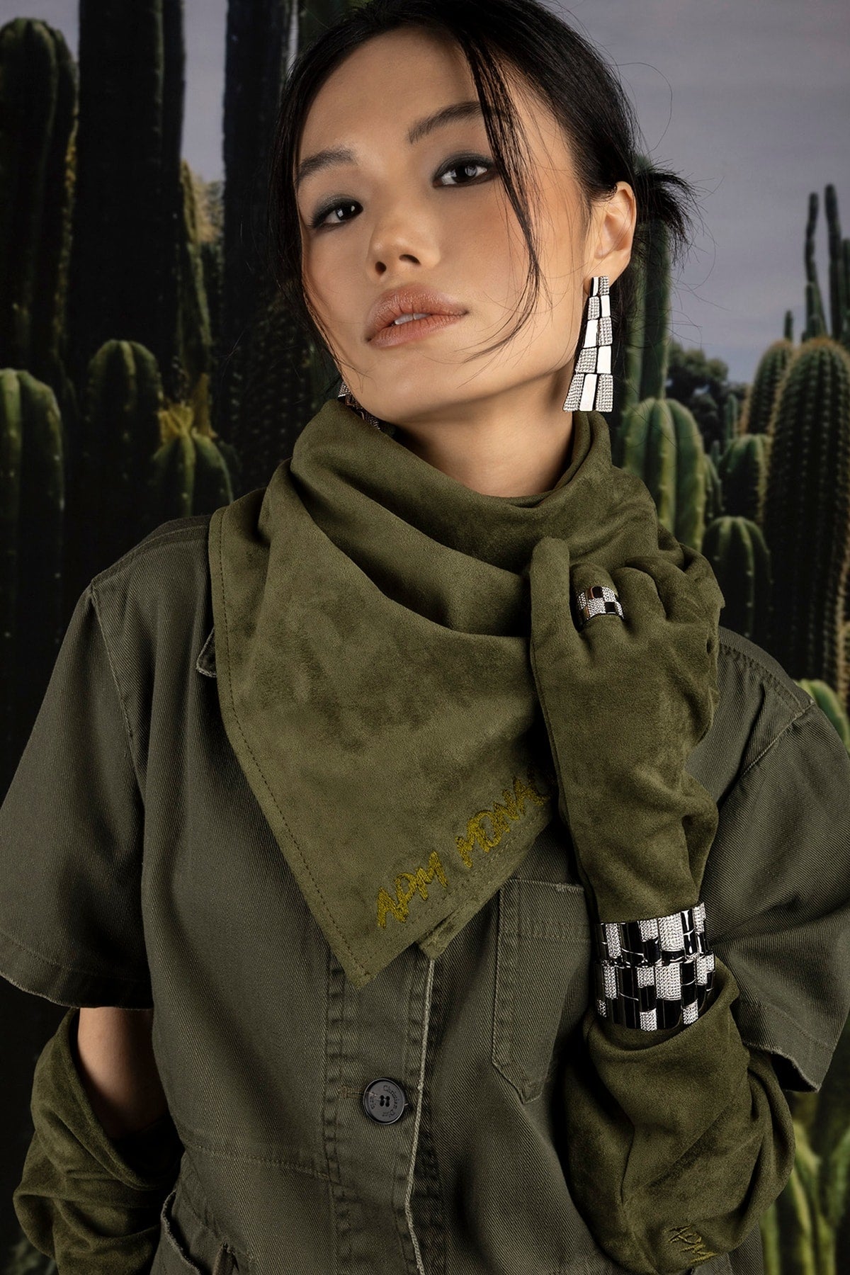 Model wearing a green jacket and scarf with cactus background