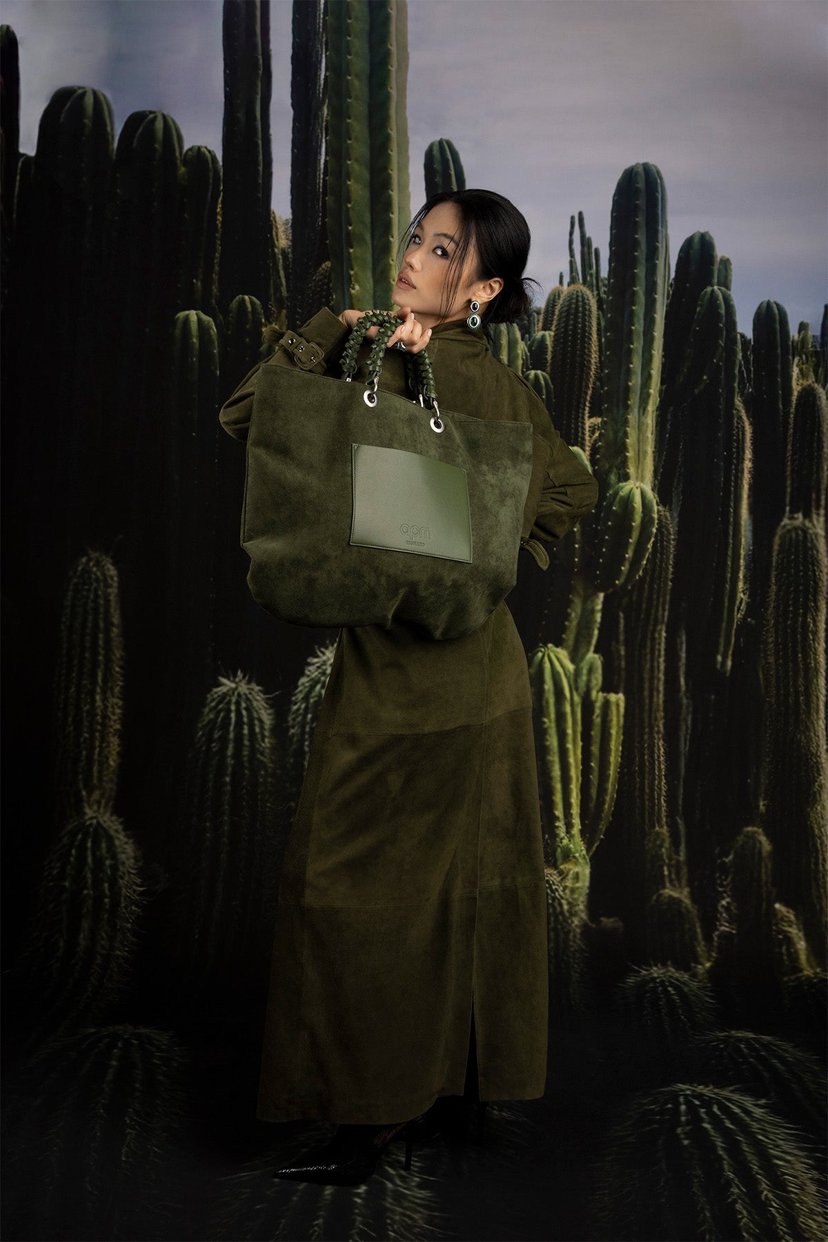 Model holding a green bag in a cactus-filled landscape