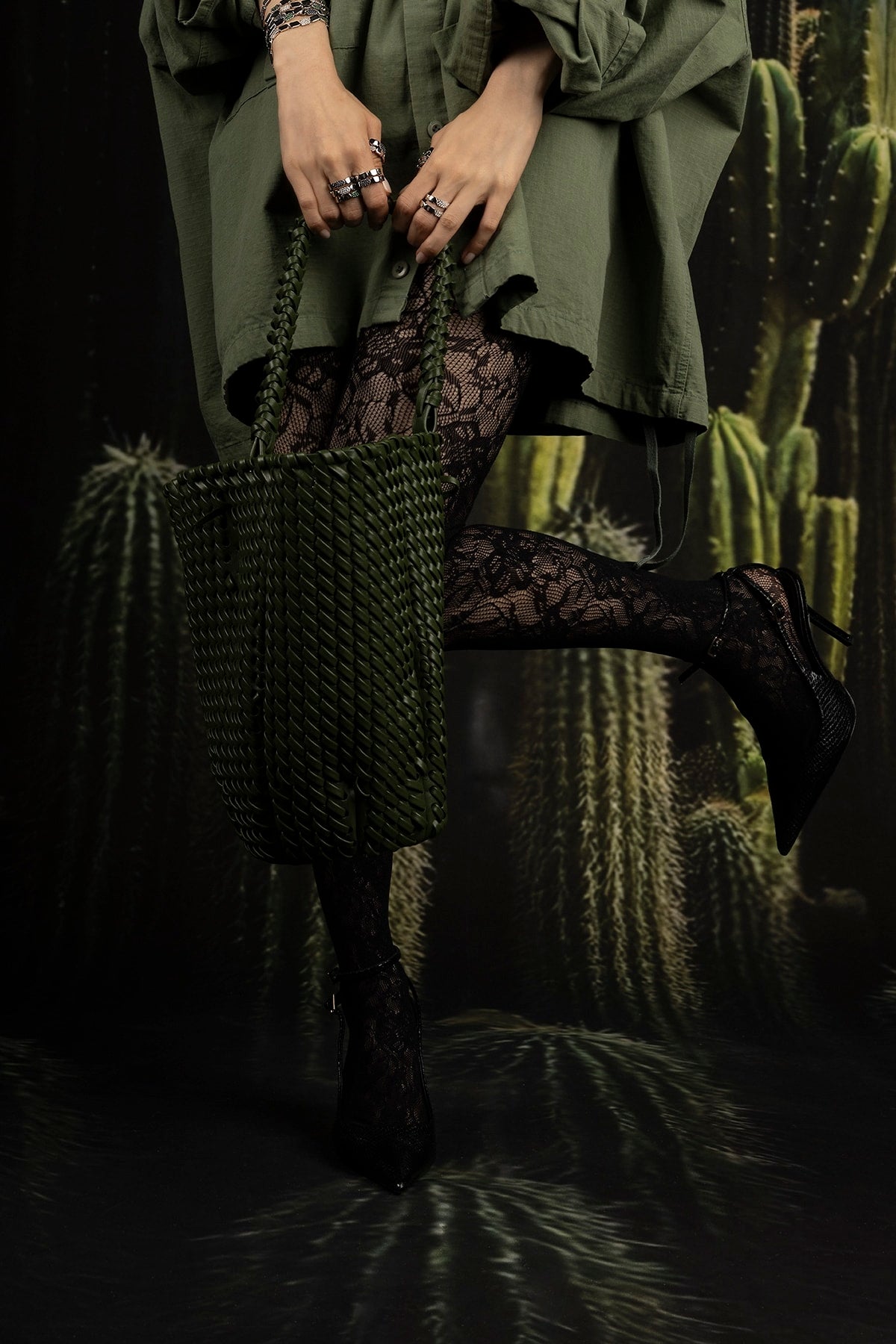 Model holding a textured green bag with cactus plants in the background