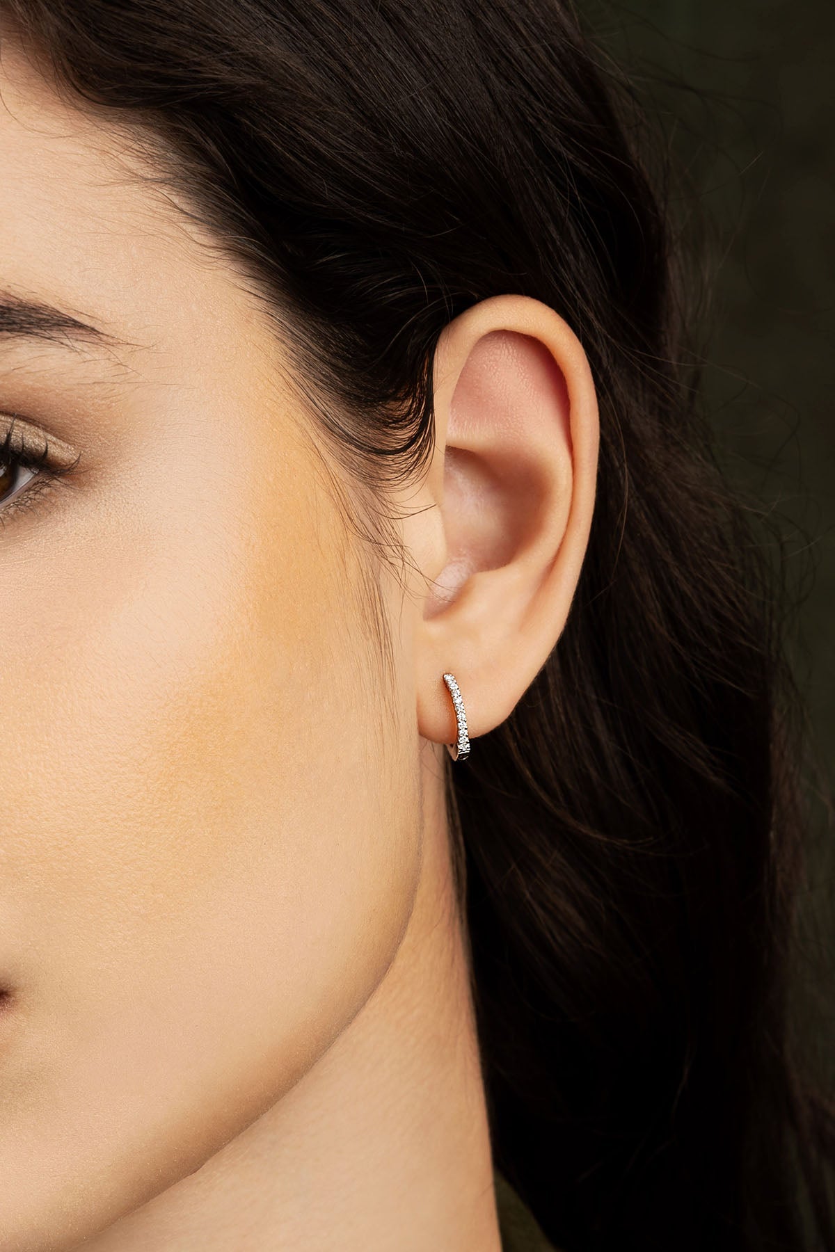 Close-up of a woman's ear wearing a earring against a dark background