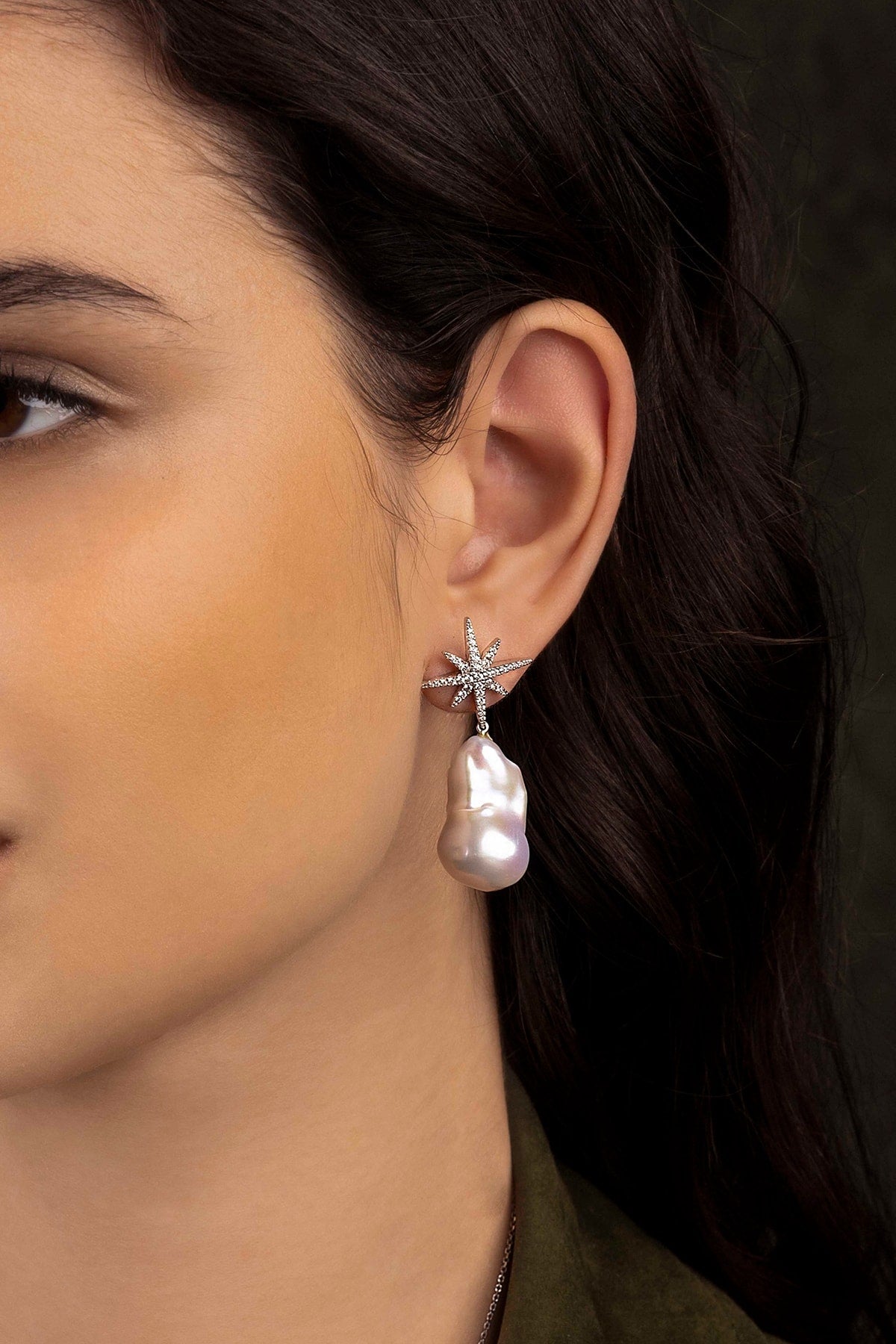 Close-up of a woman wearing a star-shaped earring and pearl drop earring.