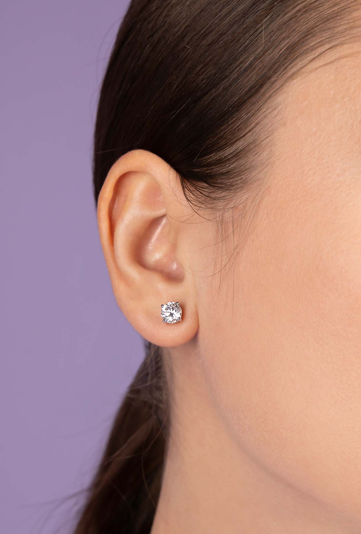 Close-up of an ear wearing a diamond earring against a purple background