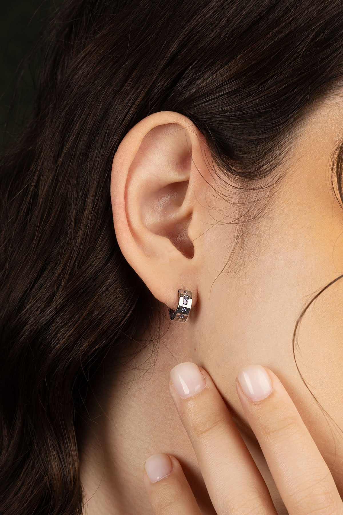 Close-up of an ear wearing a small earring with a hand touching the jawline.