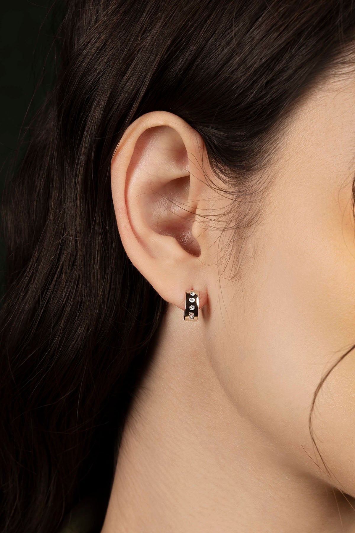 Close-up of an ear wearing a small black and white earring against a dark background