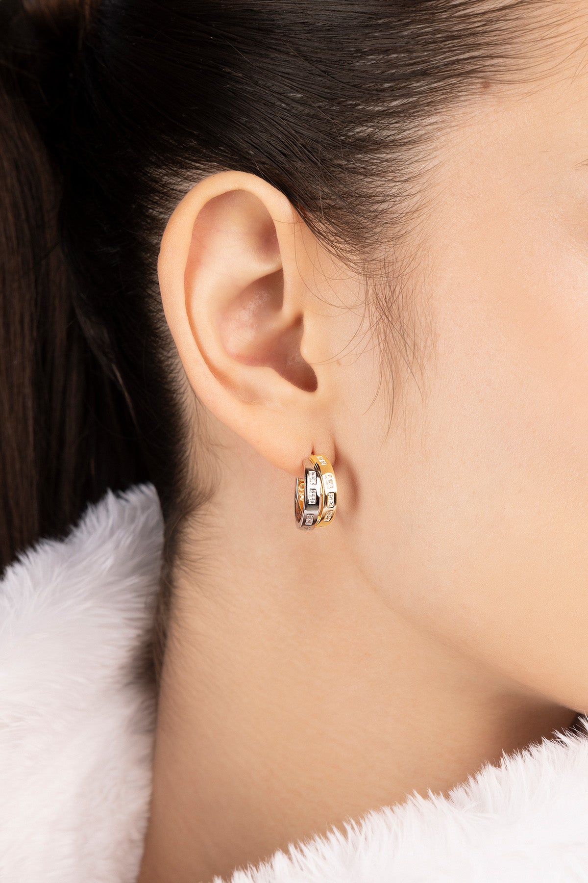 Close-up of a person wearing gold hoop earrings with a white fur collar.
