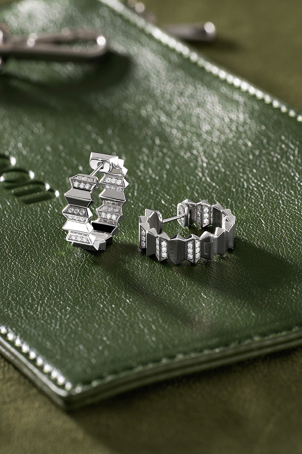 Silver hoop earrings on a green leather surface