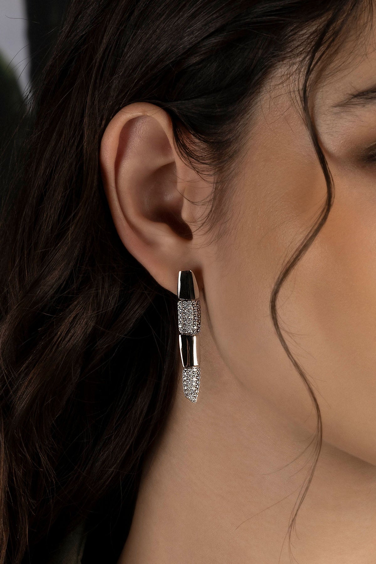 Close-up of a model wearing a silver earring with a dark background