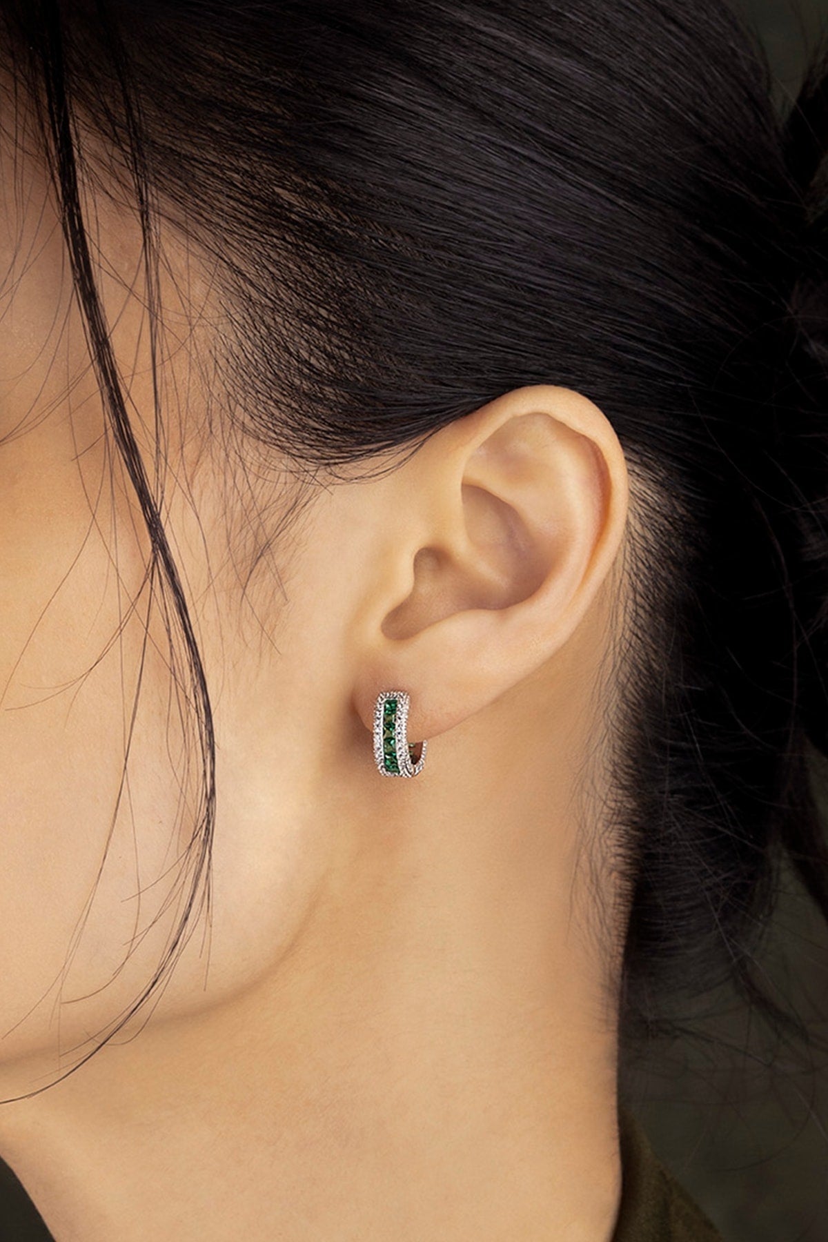 Close-up of an ear wearing a green and silver huggie earring