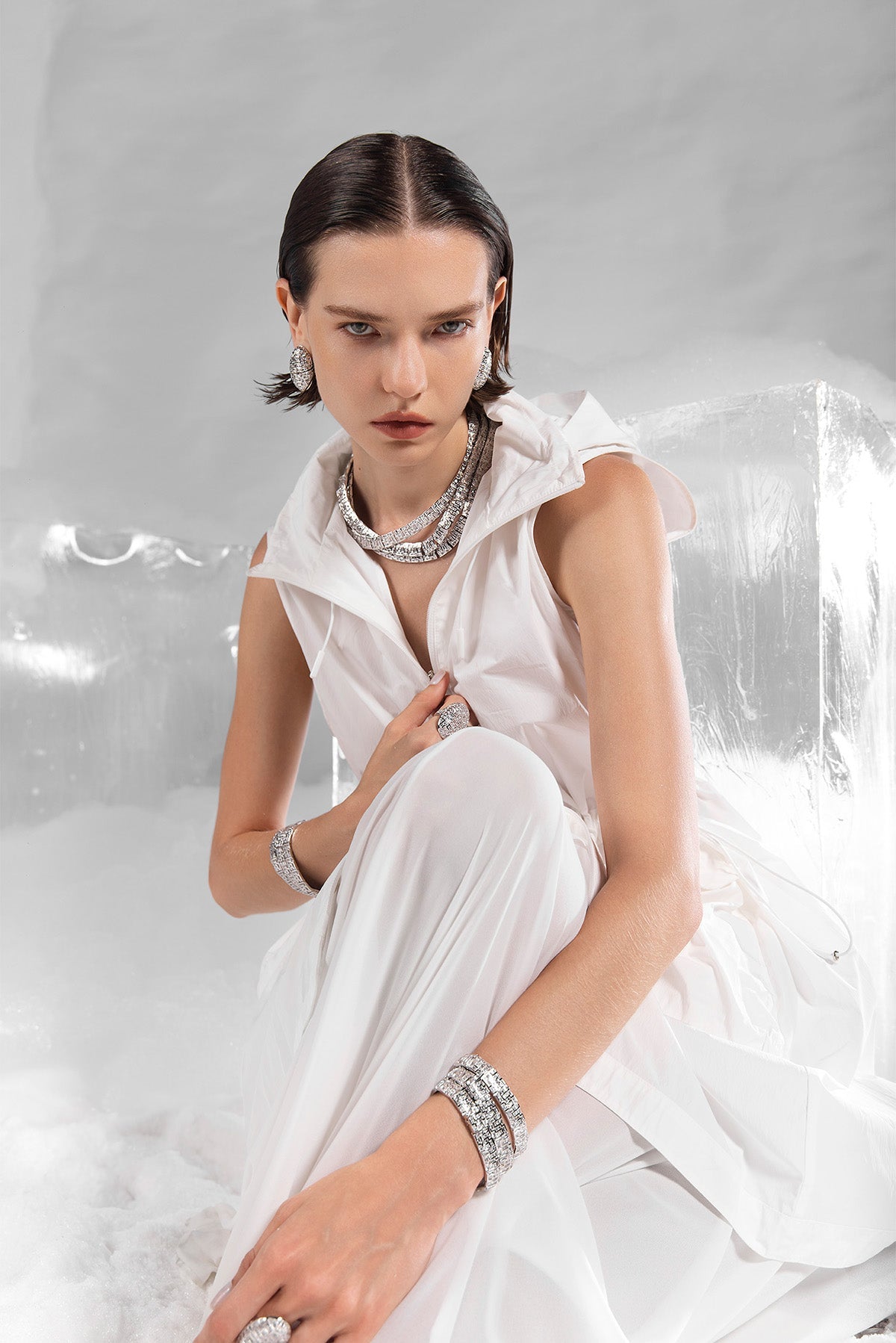 Woman in a white dress with APM MONACO statement labyrinth jewelry sitting on a white surface