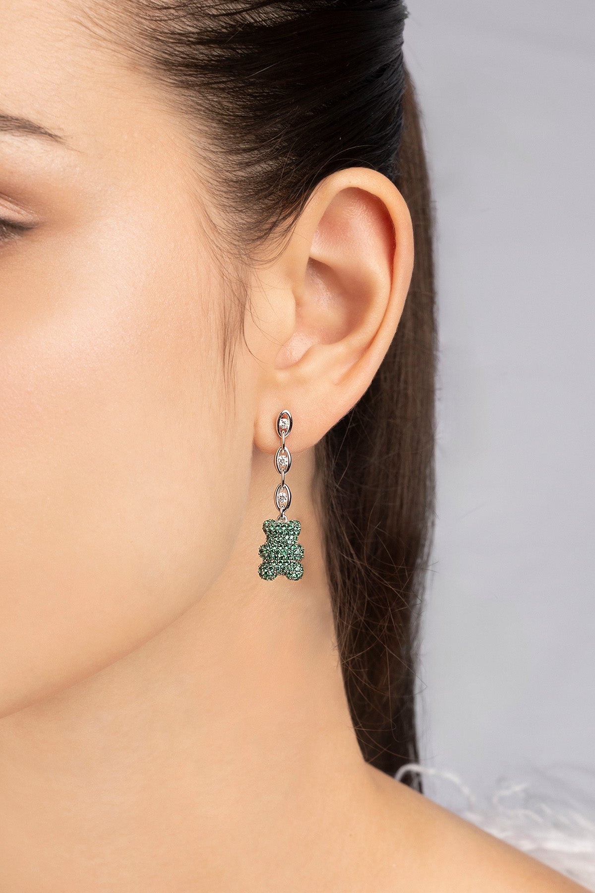 Close-up of a person wearing mint yummy bear drop earrings from APM MONACO with a neutral background